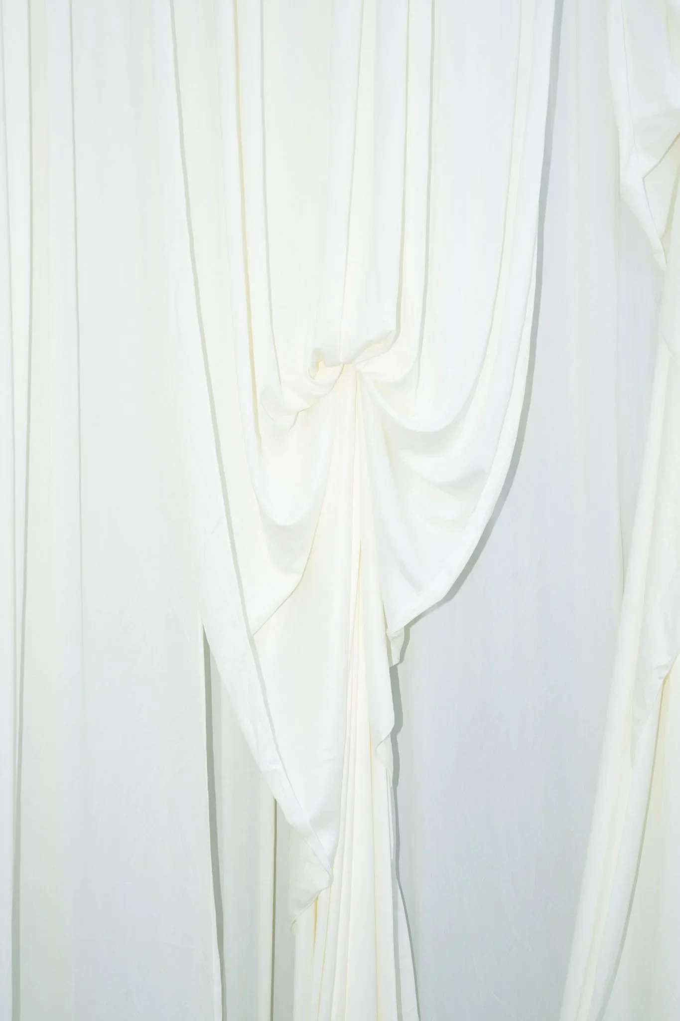 Close-up of white fabric, possibly curtains or drapes, with pleats and flowing folds.