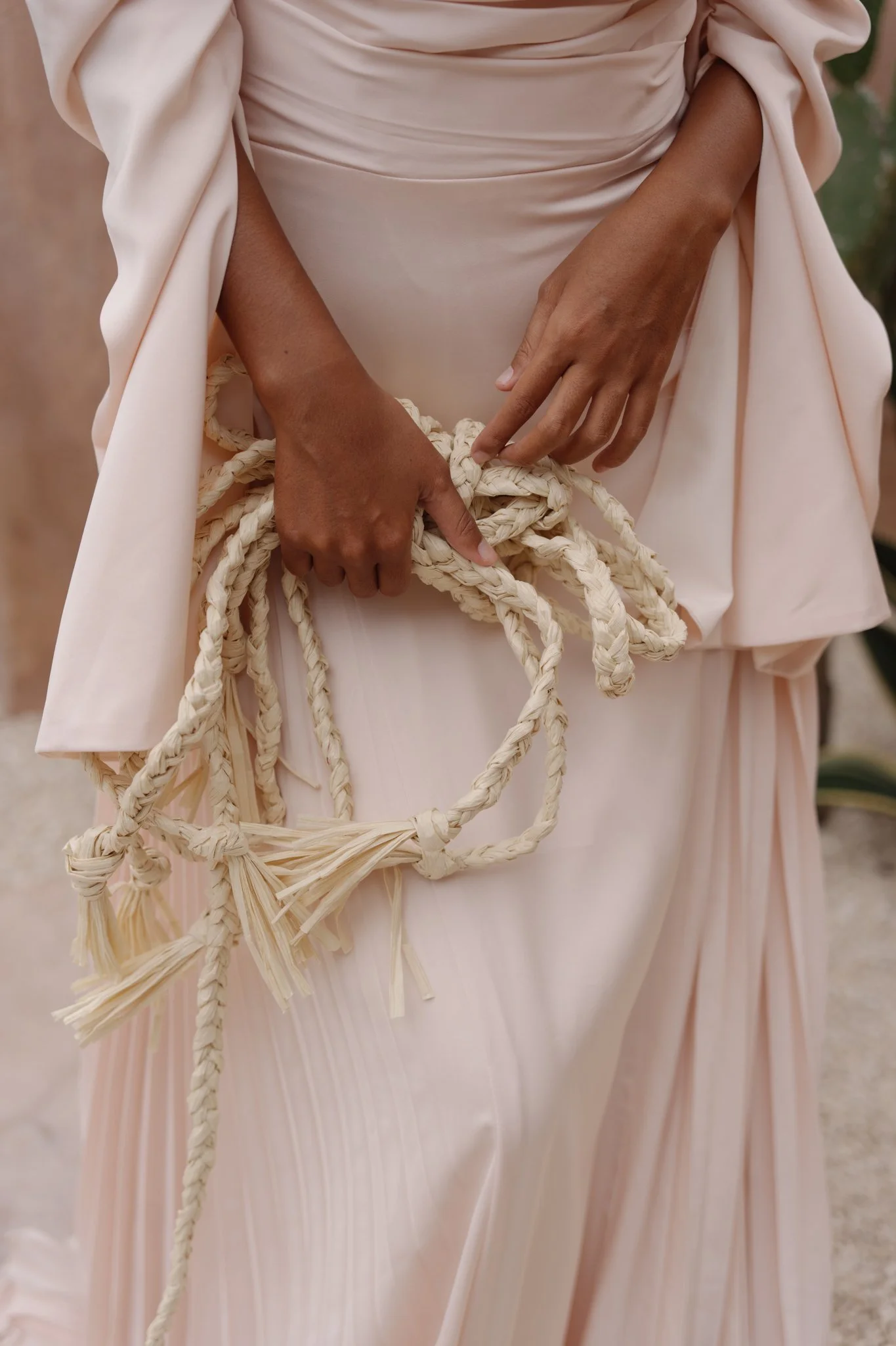 Close-up of a person wearing a light pink or cream-colored garment, holding a braided rope or cord with both hands.