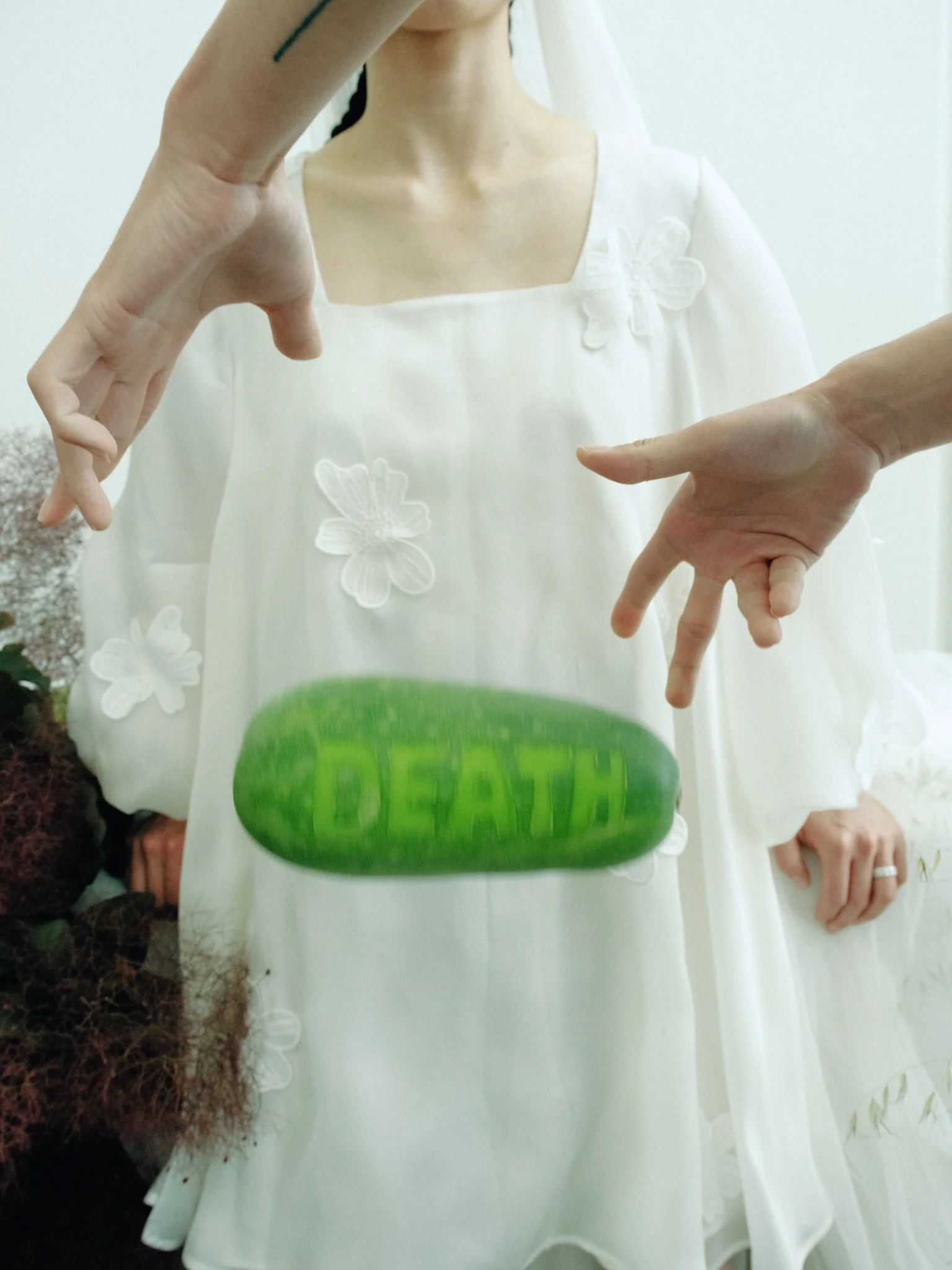 Person wearing a white dress with floral designs, holding a watering can, with soil and plants nearby.
