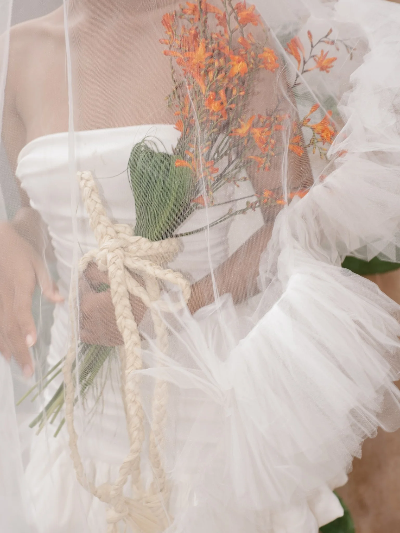 Close-up of white fabric with orange flowers and green leaves, viewed through a sheer white curtain or overlay.