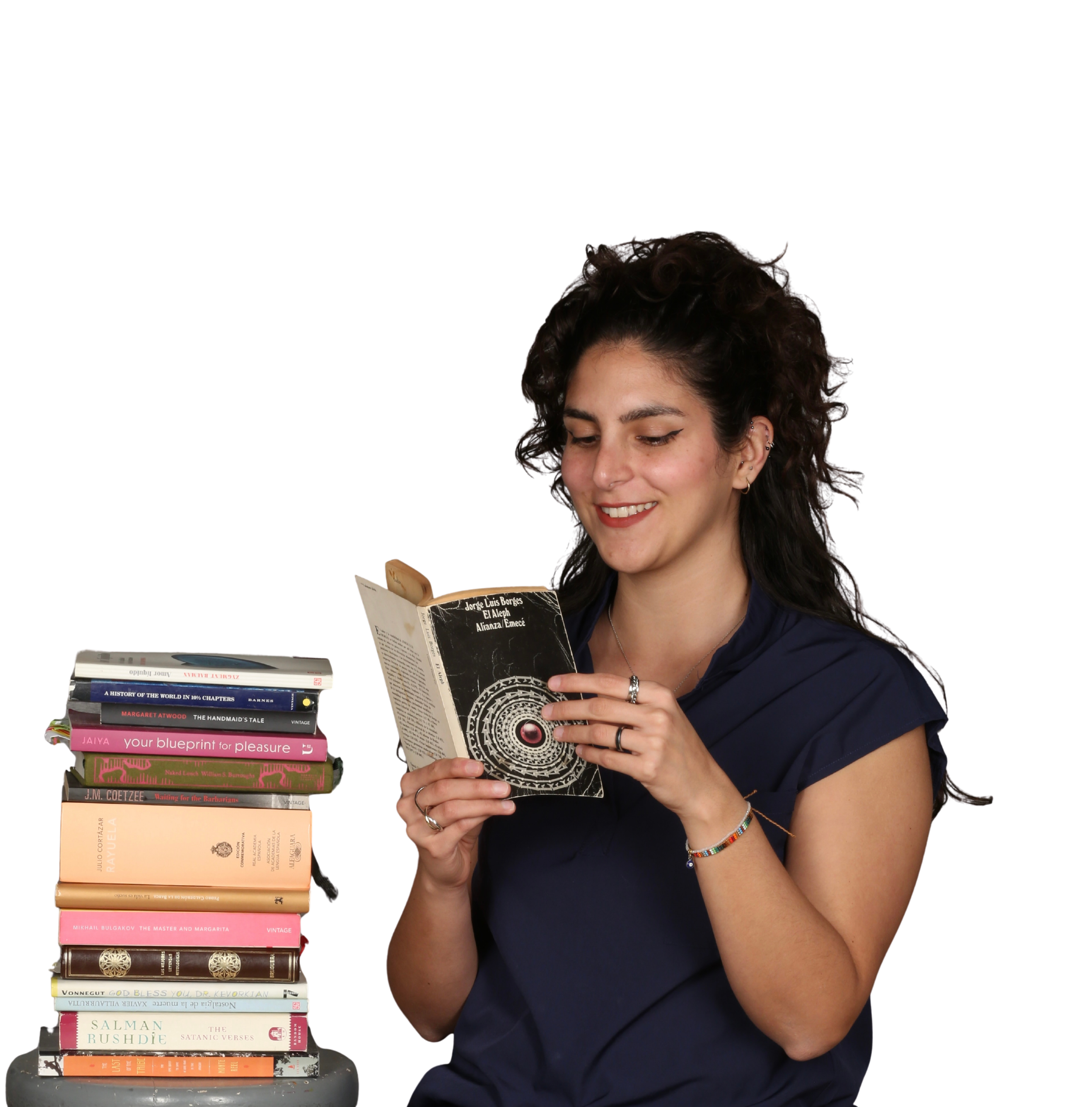 Una joven con pelo rizado y de piel clara lee un libro. A su lado hay una pila de libros apilados en una mesa. Ella lleva puesta una camiseta azul y tiene accesorios estilizados en las orejas y en la muñeca. La escena muestra un ambiente de lectura.