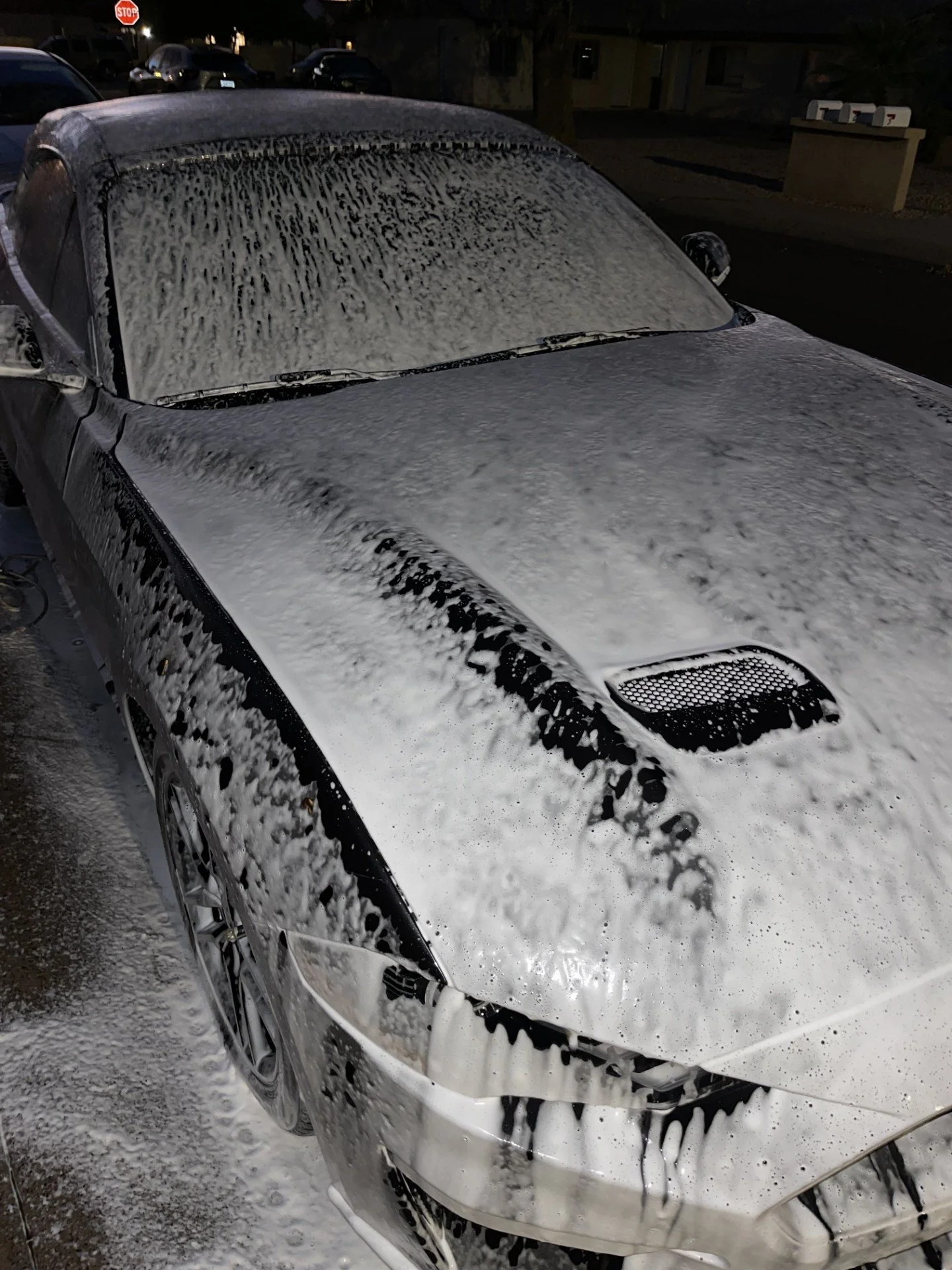 A silver car covered in soap suds during cleaning at night in a parking lot.