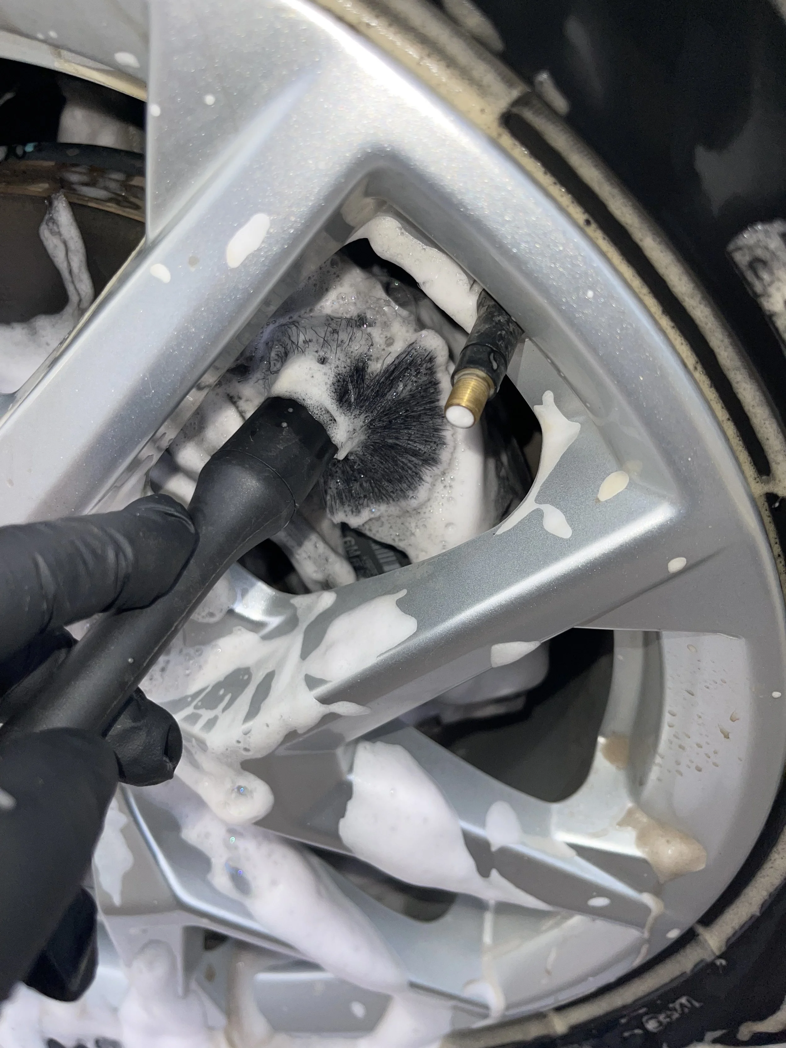 Cleaning a car wheel with a brush and soapy foam.
