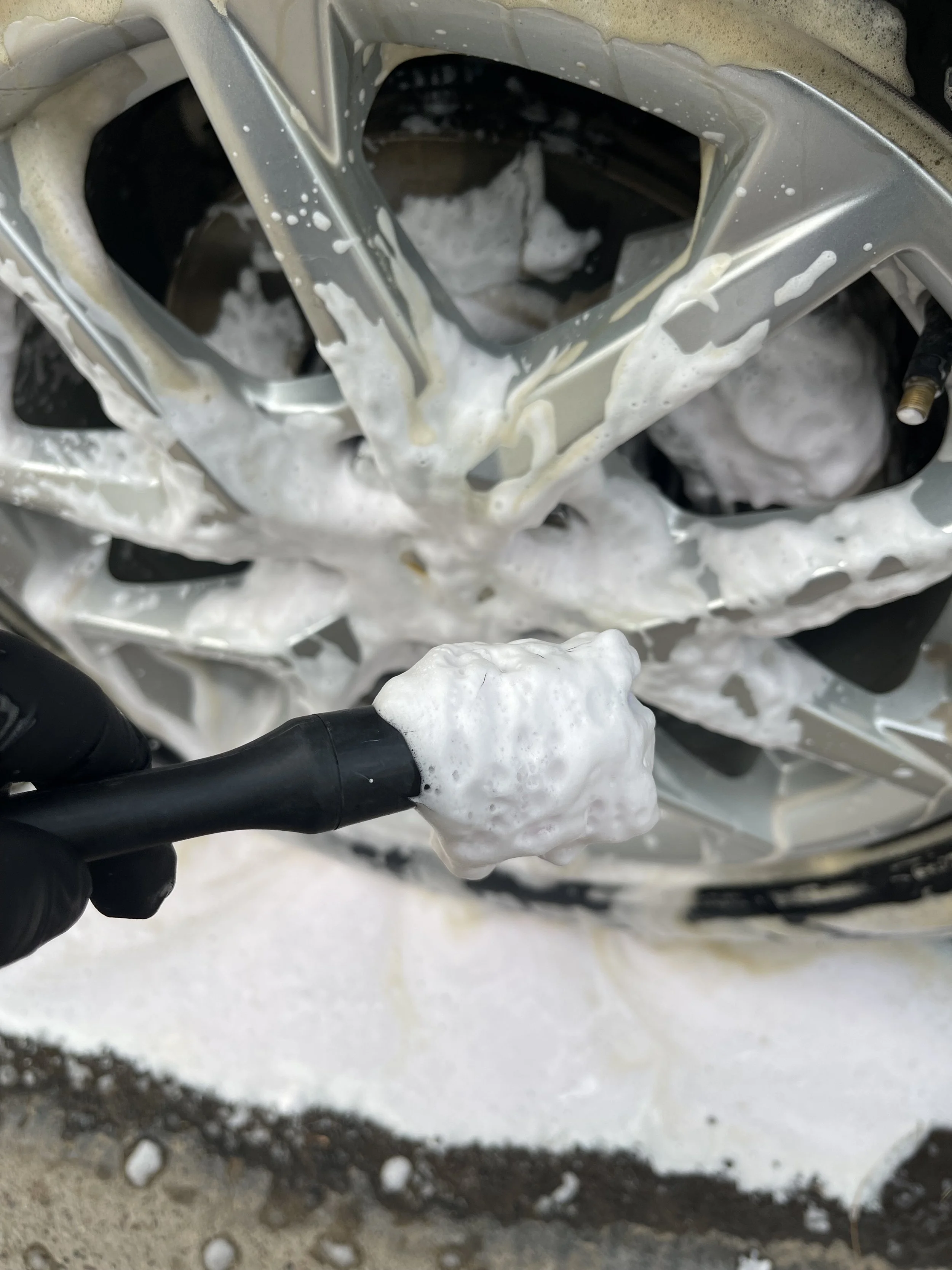 Close-up of a car's wheel with soap suds and foam during cleaning.