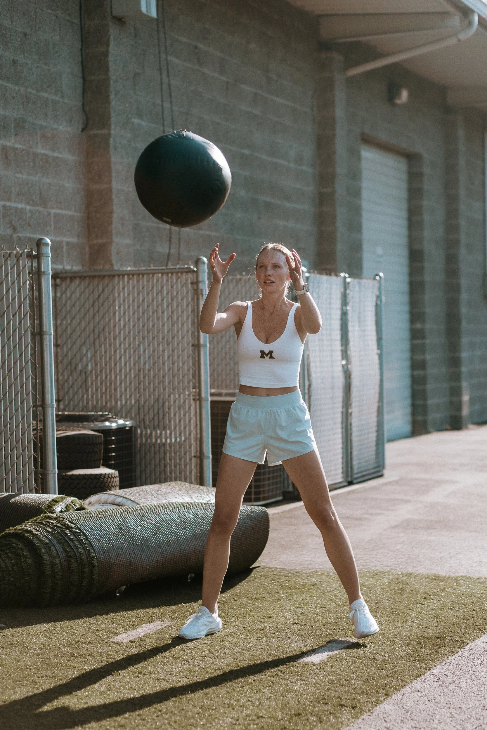 A Dropgym member in athletic gear tossing a medicine ball in an outside of the gym.