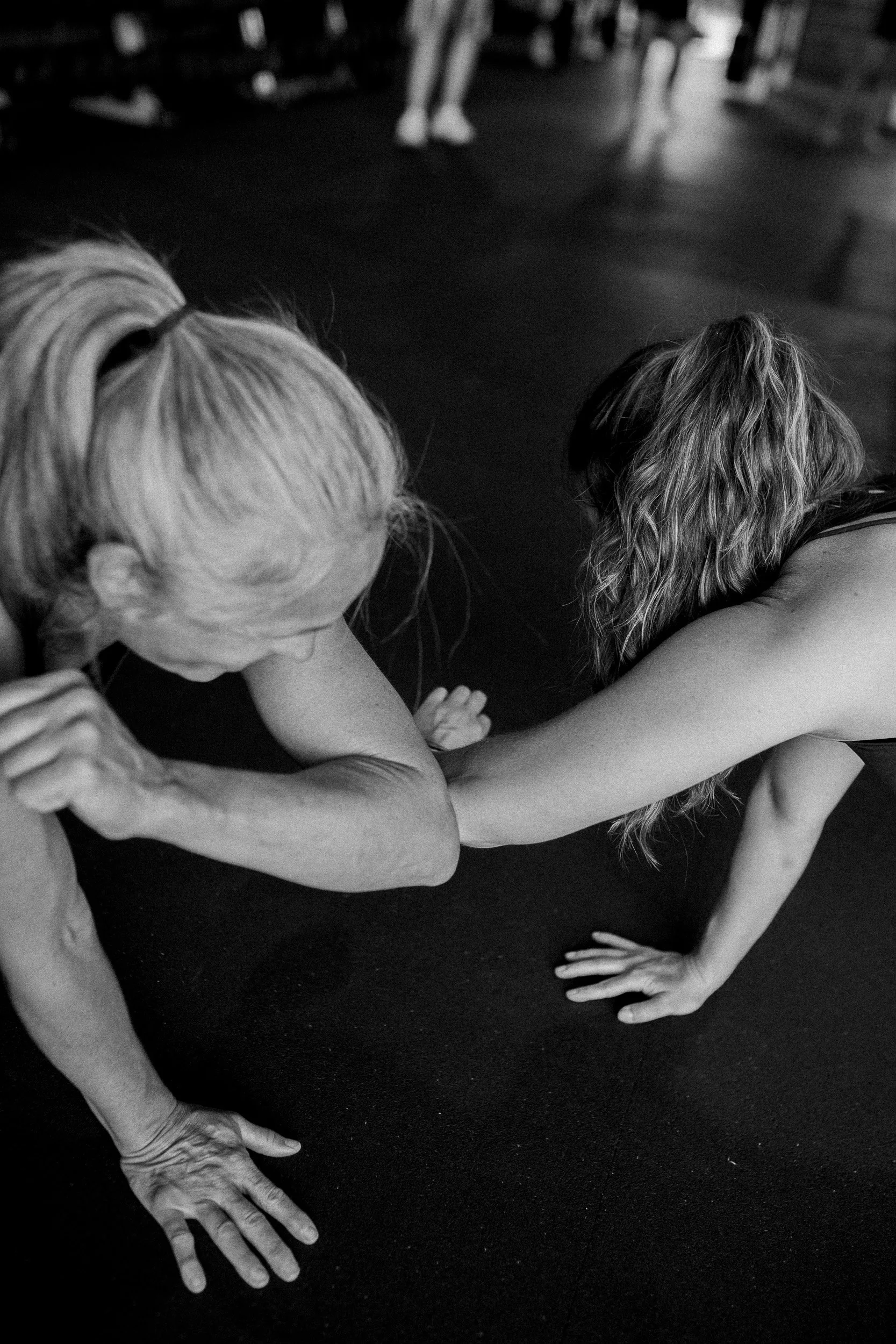 Two women in a Dropgym class in a plank laughing and touch elbows.