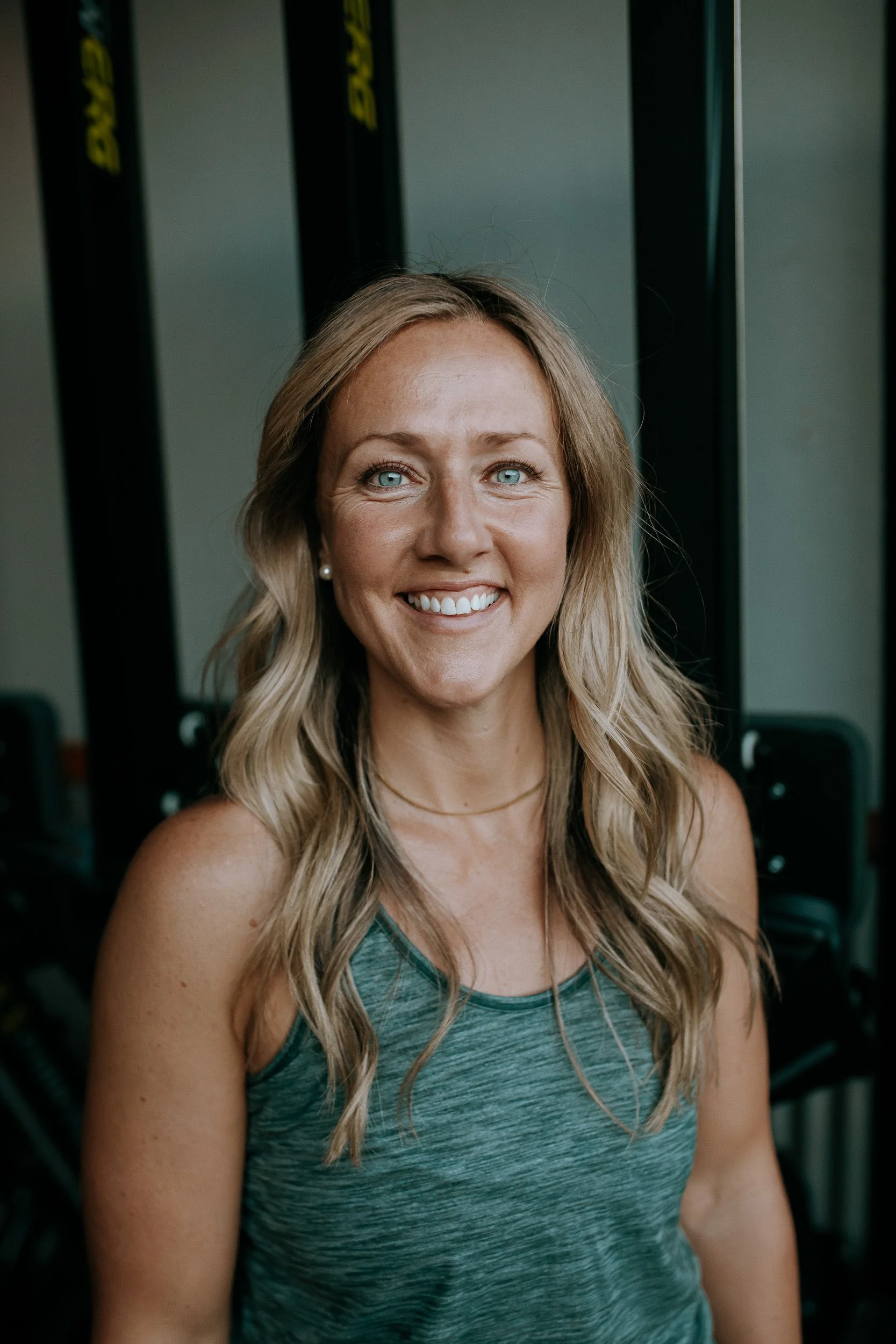 Shantell, co-founder of Dropgym in Southern Oregon, wearing a gym tank top, with gym equipment in the background and smiling at the camera.