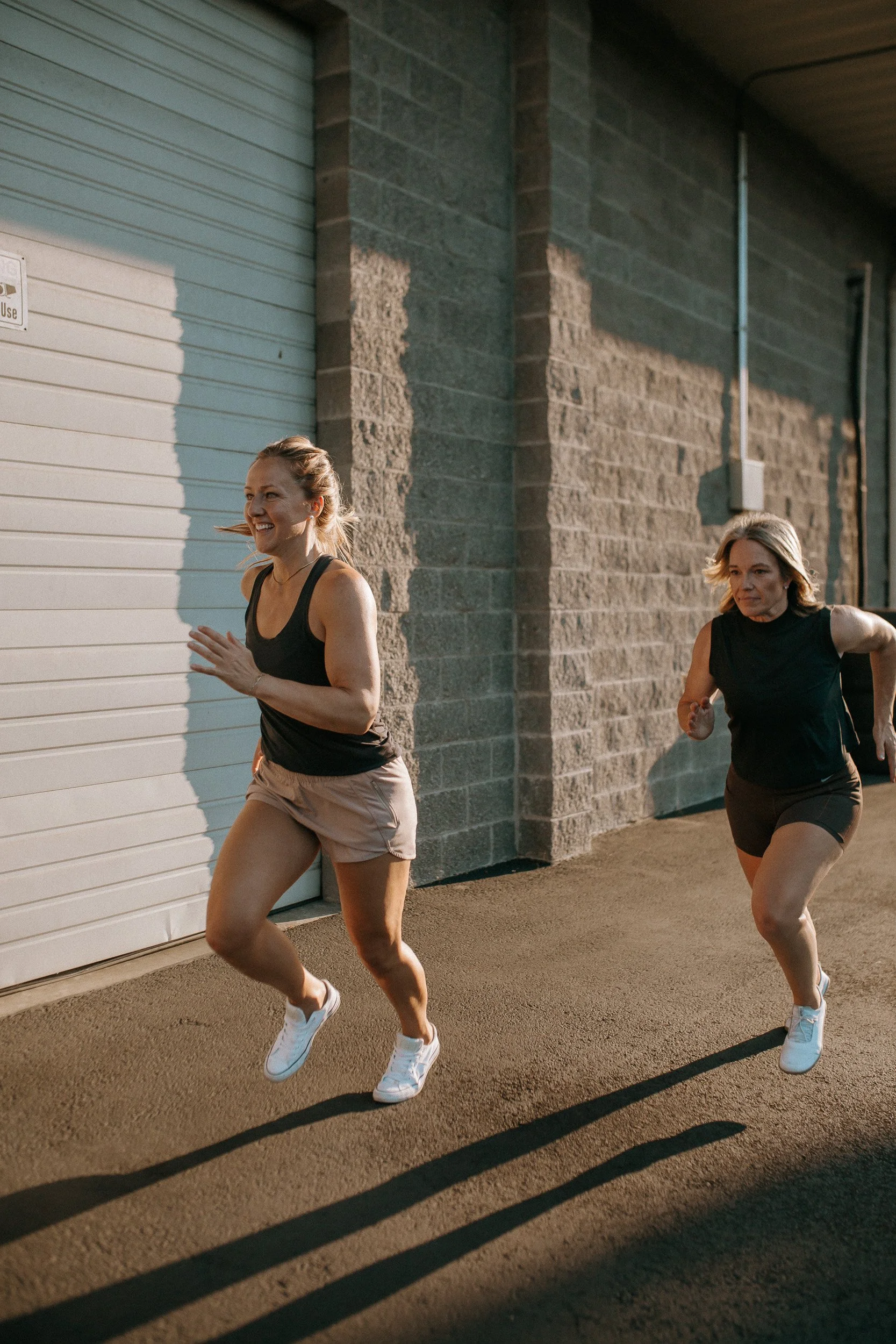 Lu and Shantell are running outdoors behind Dropgym during sunset, casting long shadows on the ground.