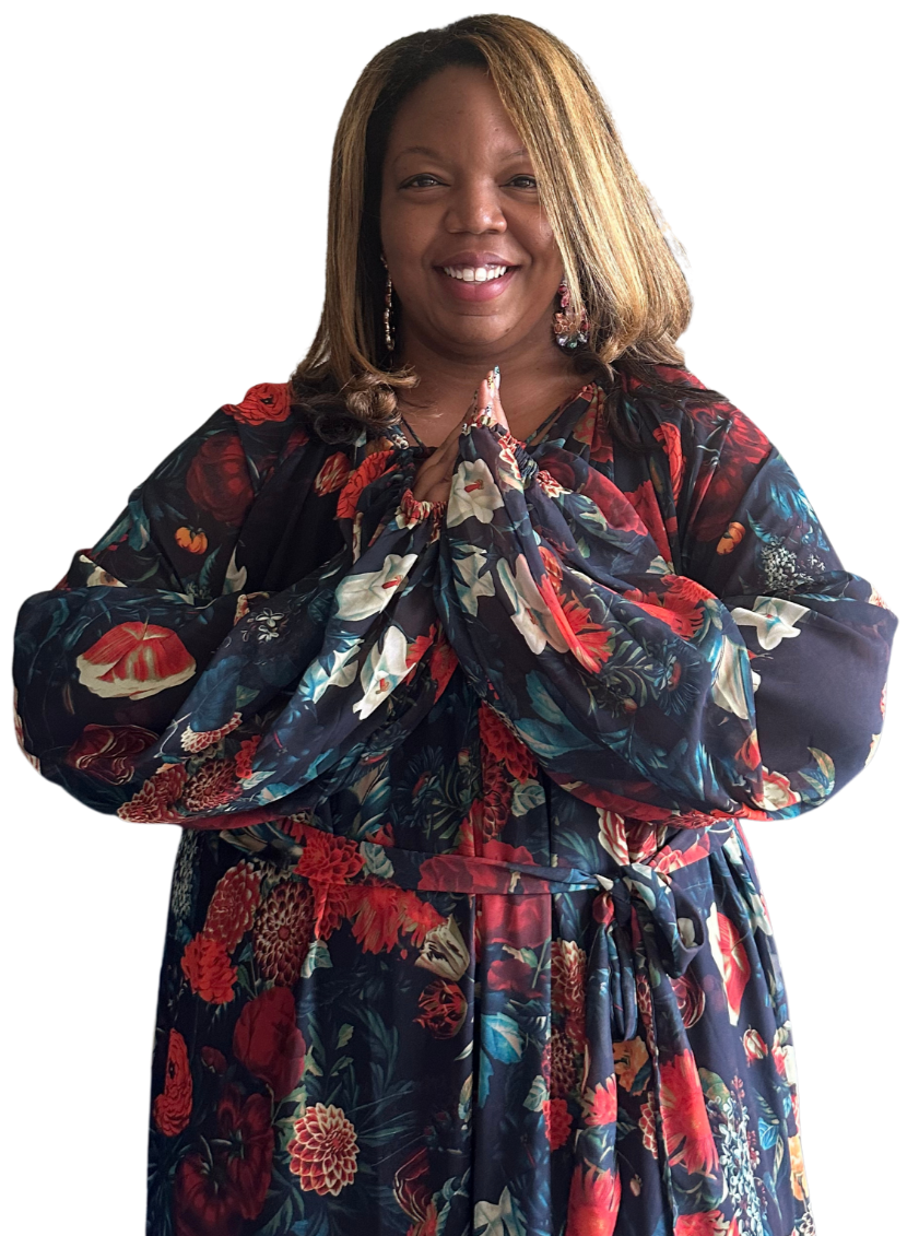 A woman smiling with her hands pressed together in a prayer position, wearing a floral dress with rich reds, blues, and whites.