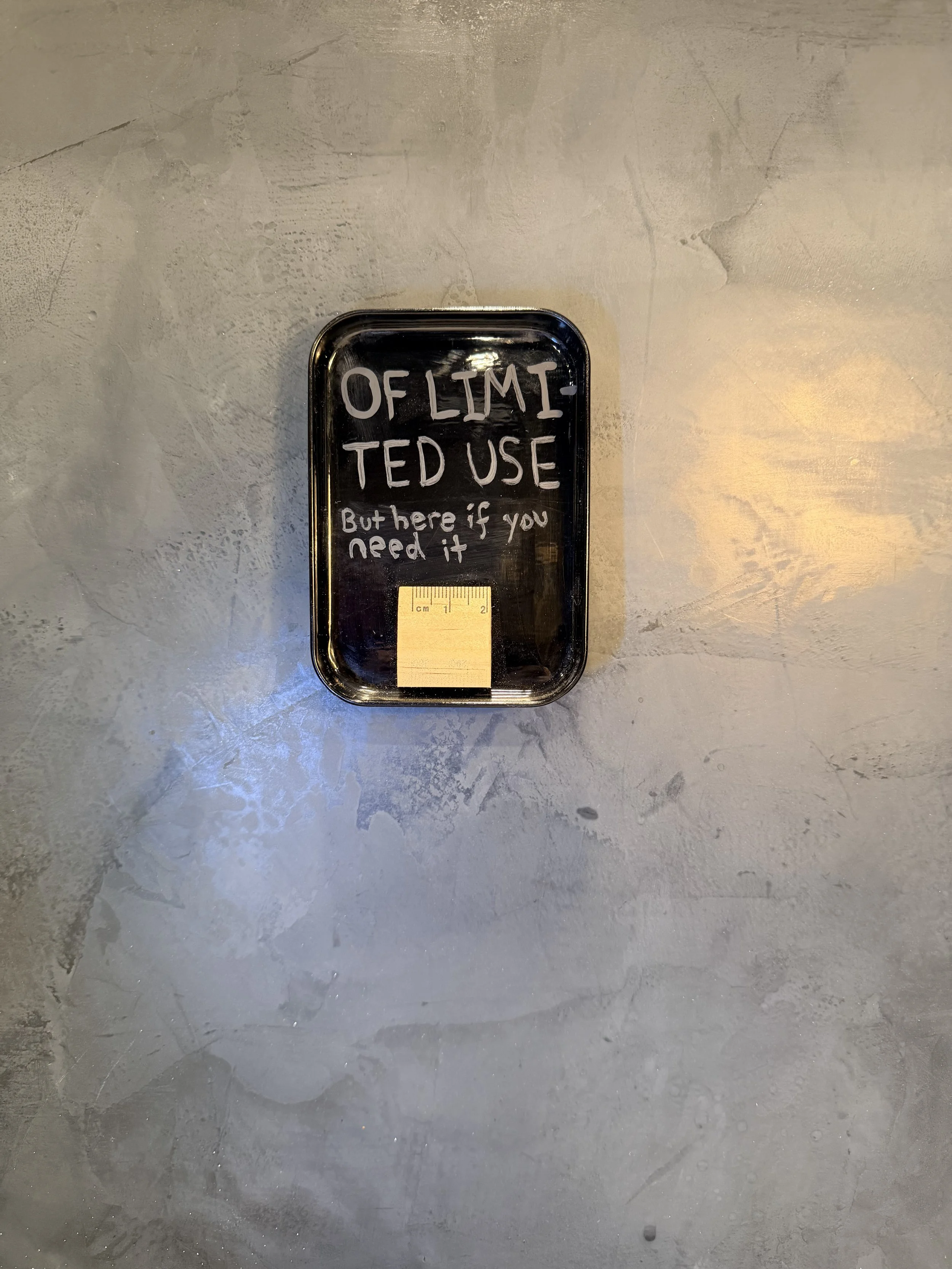 A black tray with a handwritten message that says 'OF LIMIT TED USE But here if you need it' on a textured gray surface.
