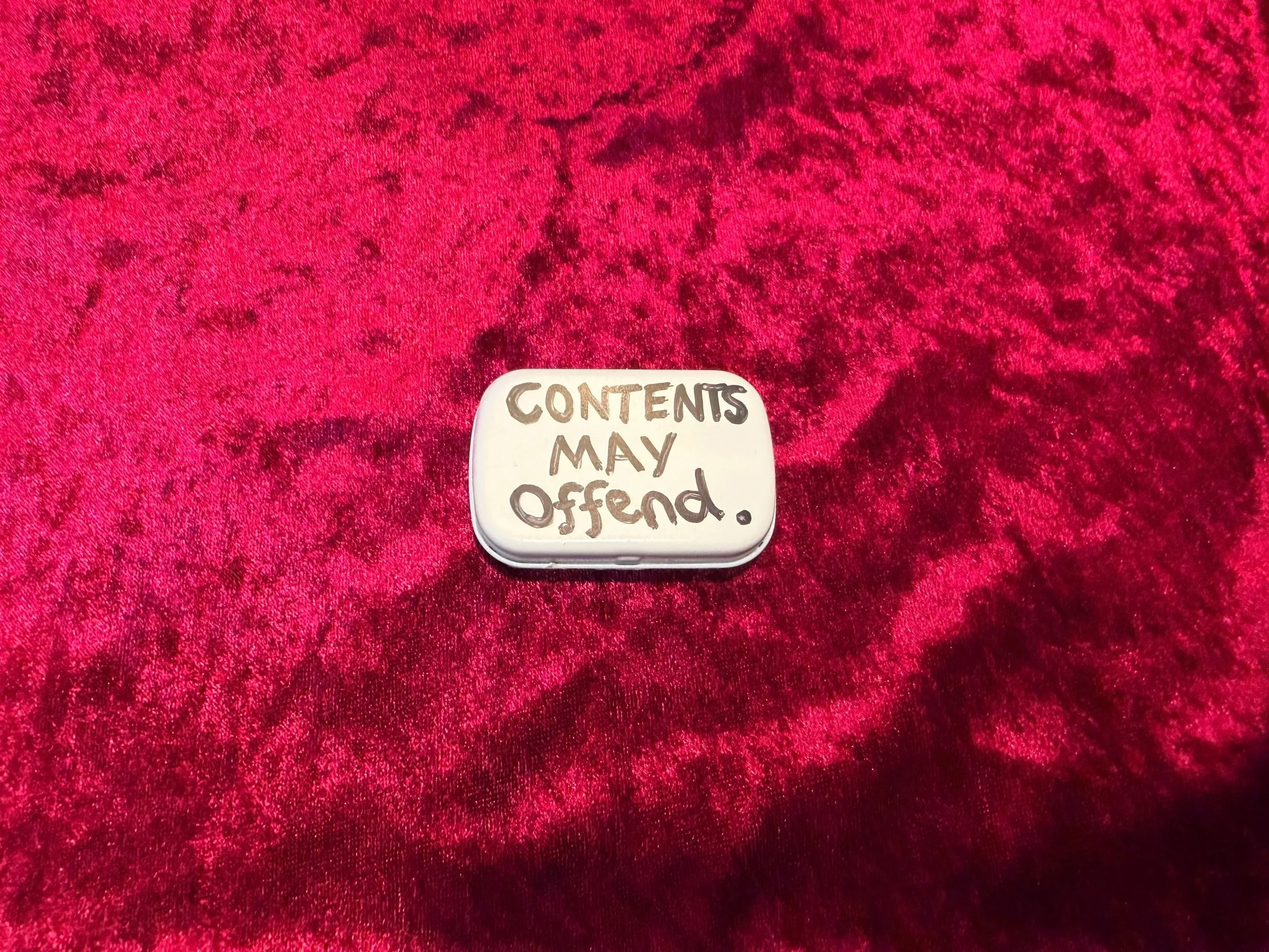Round white container with handwriting that reads: 'CONTENTS MAY OCCUR' on a red textured surface.