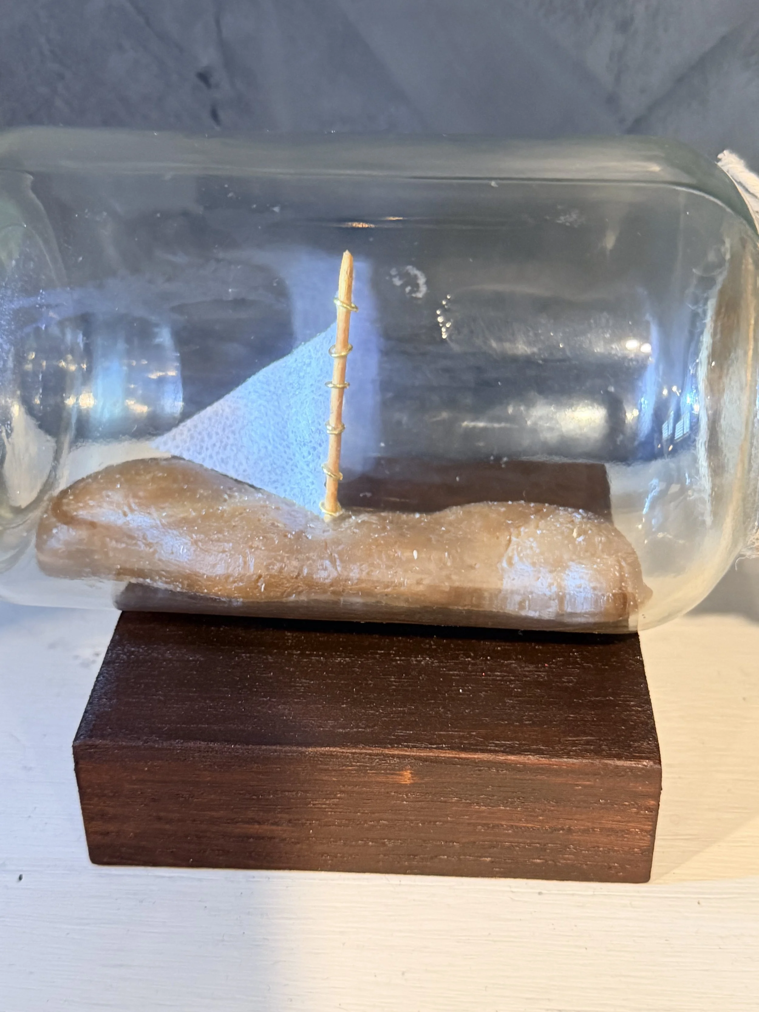 A small wooden platform with a piece of foam and a handmade paper airplane inside a clear plastic display case.