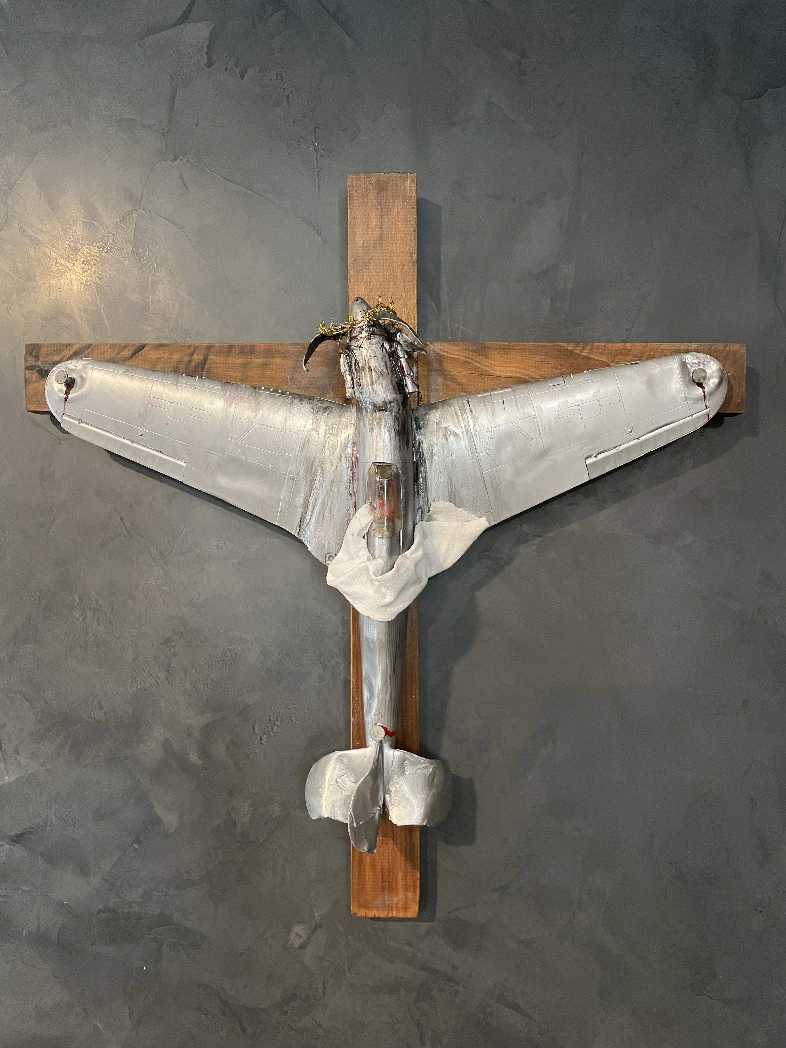 A sculpture of Jesus Christ on the cross, mounted on a wooden cross, with a dark background.