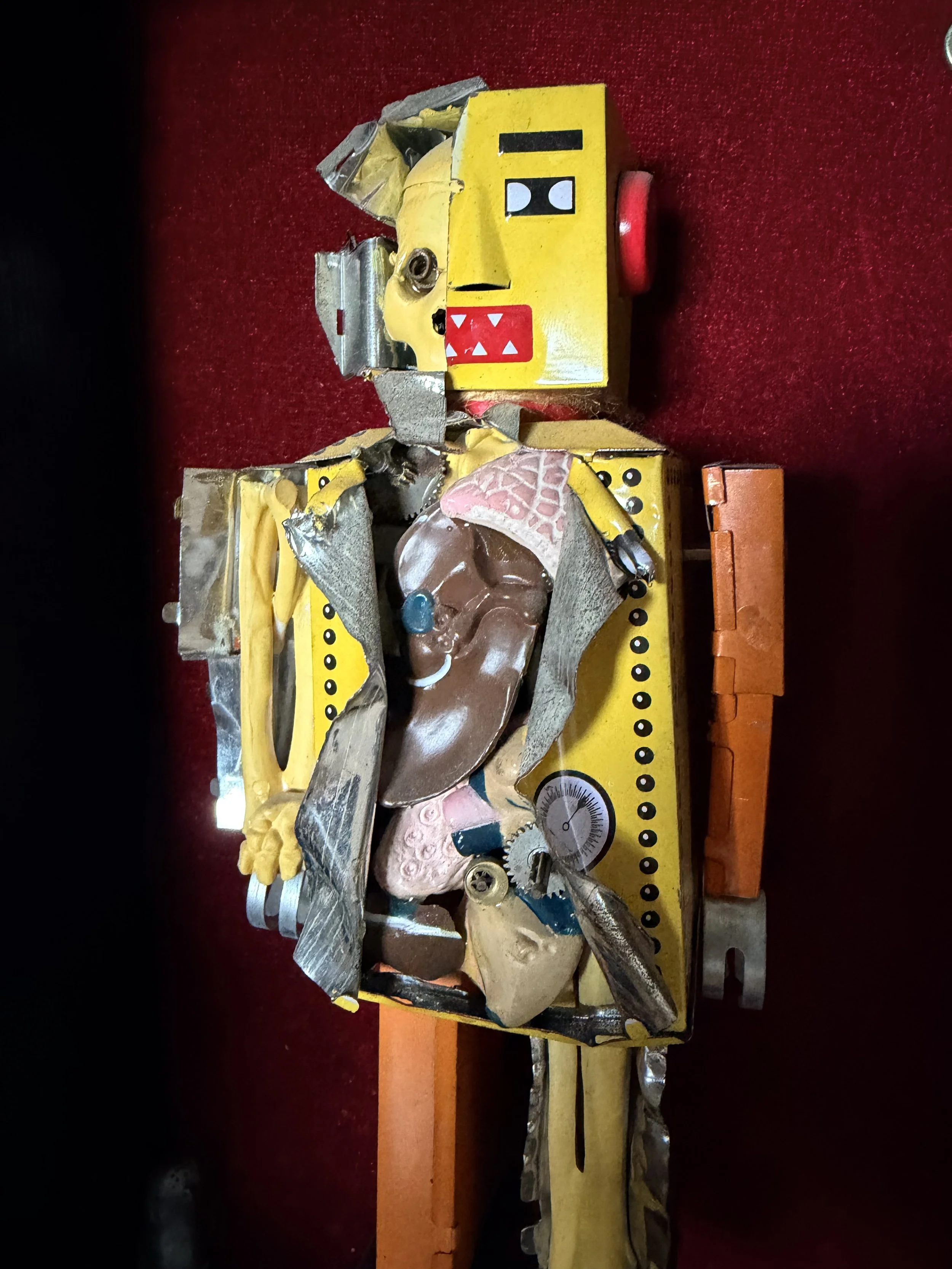 Broken mechanical toy with yellow face, red and black features, and various metal parts on red background.