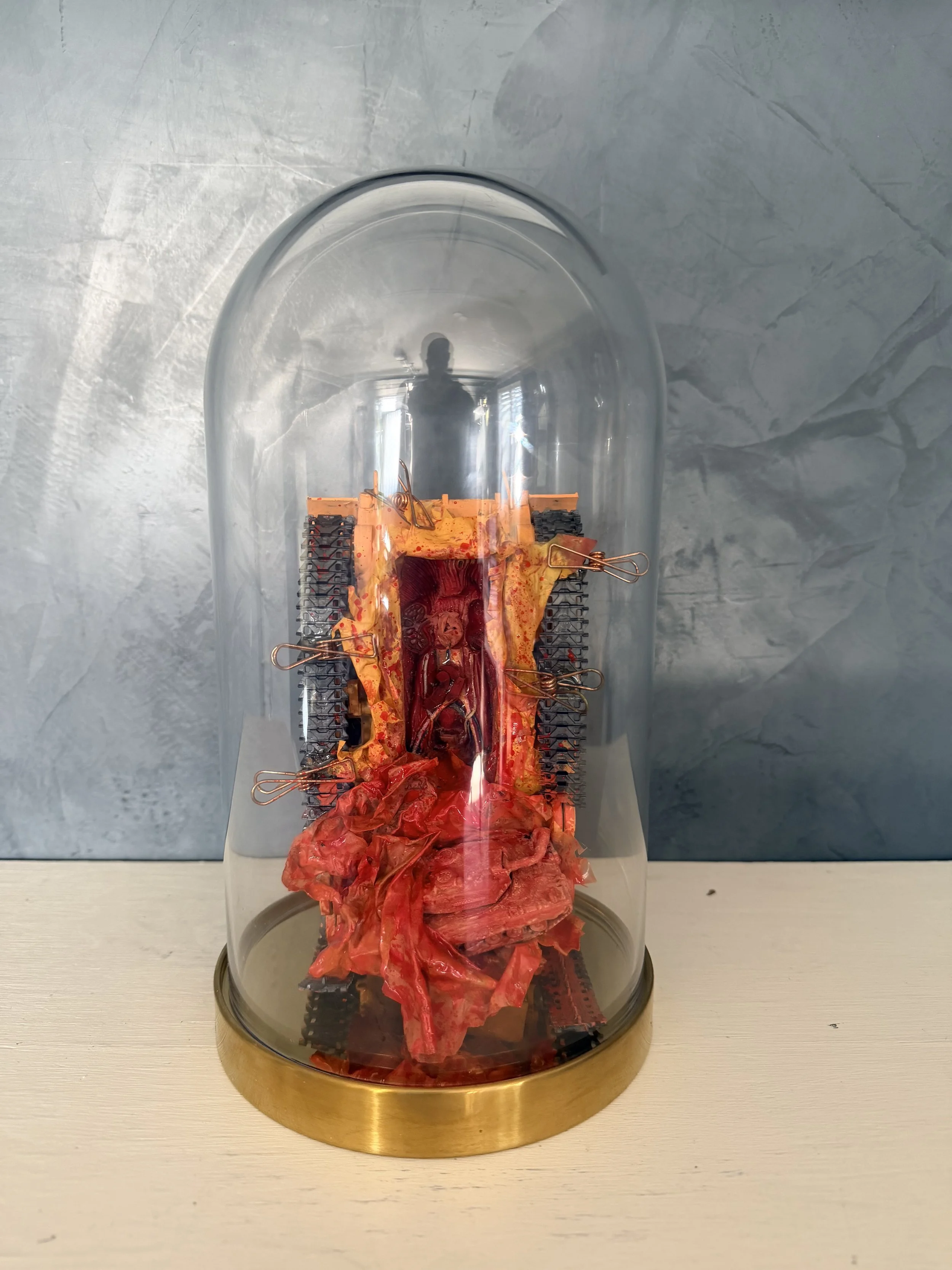 A glass dome encasing a mechanical model of human anatomy, resembling a heart and blood vessels, on a round gold base.