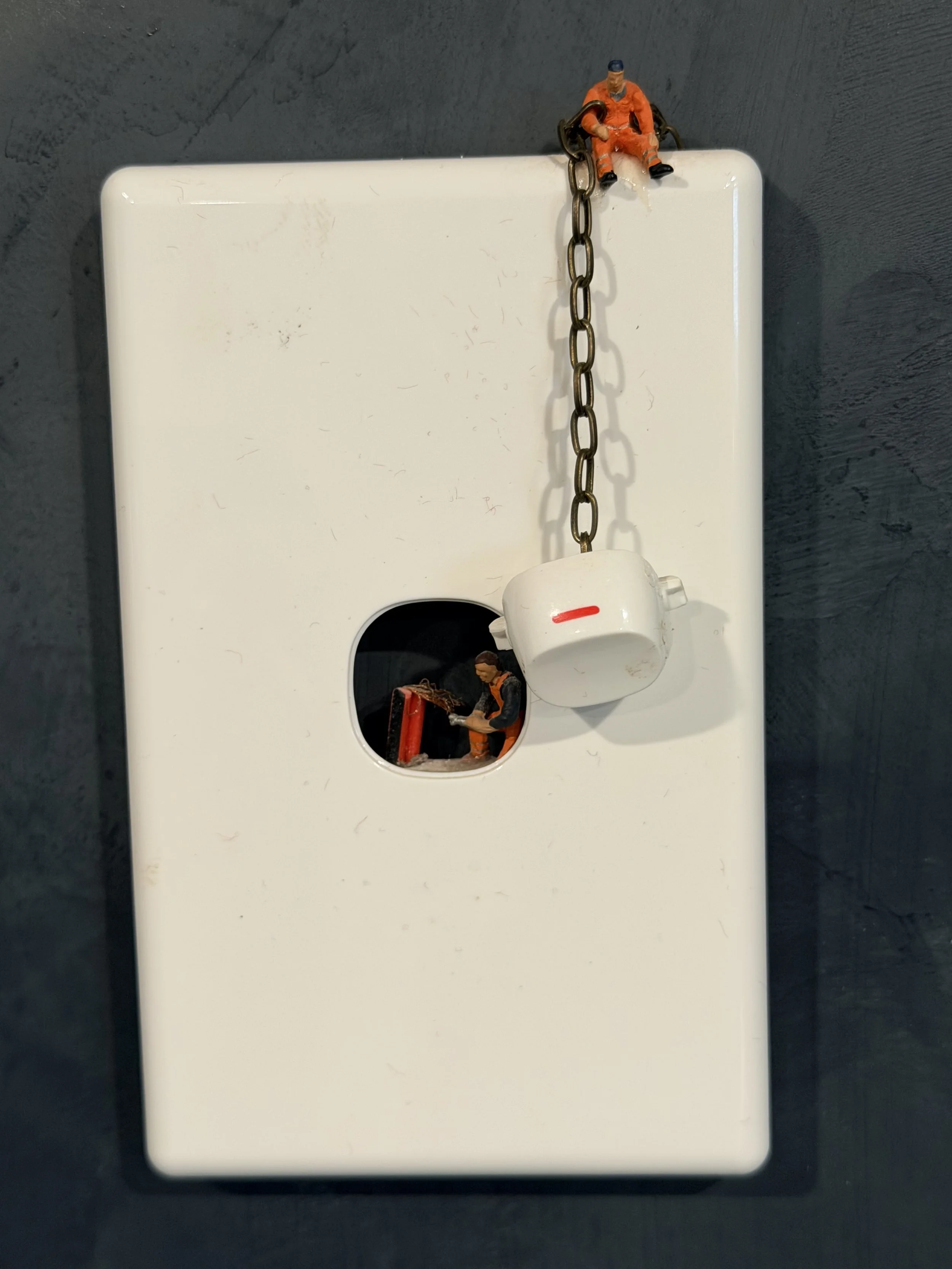Miniature figurines of two construction workers, a chain, and a white object, arranged on a flat surface with a dark background.
