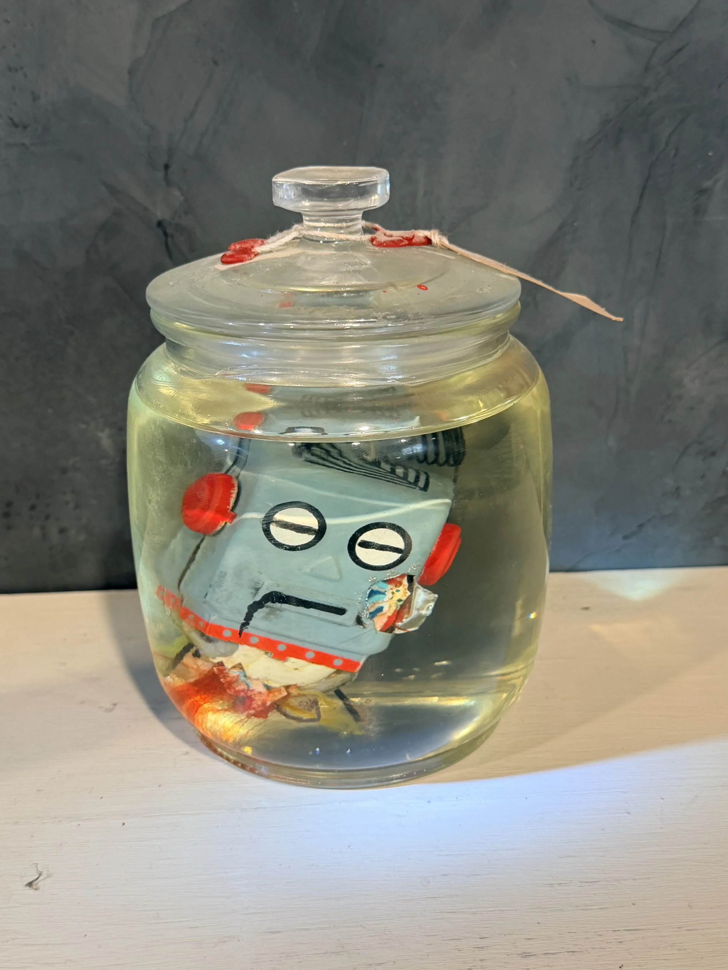 A glass jar with a lid filled with clear liquid, sitting on a white surface against a dark, textured background.