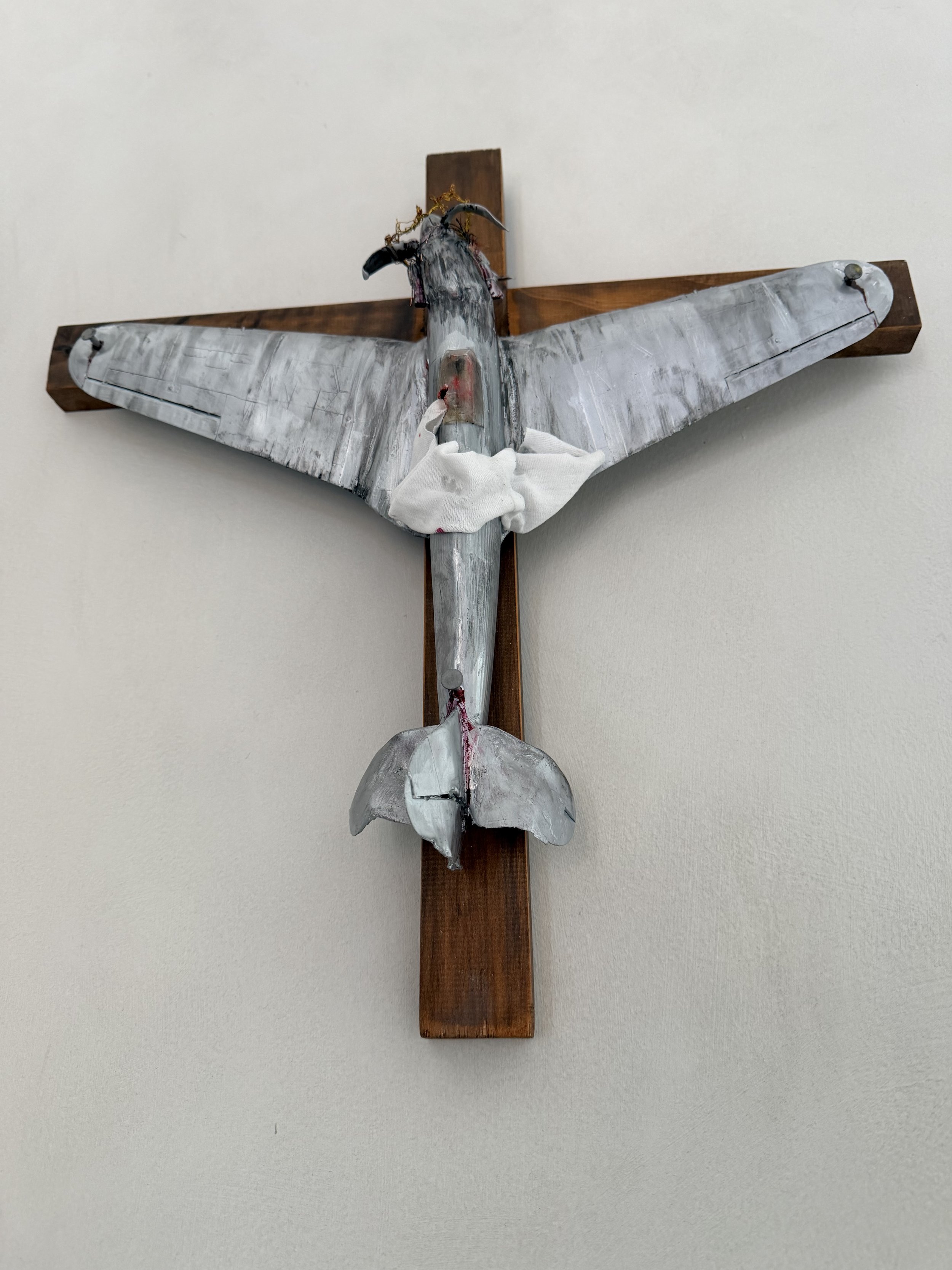 A mounted church cross with a metal dove sculpture attached to the front, positioned on a white wall.
