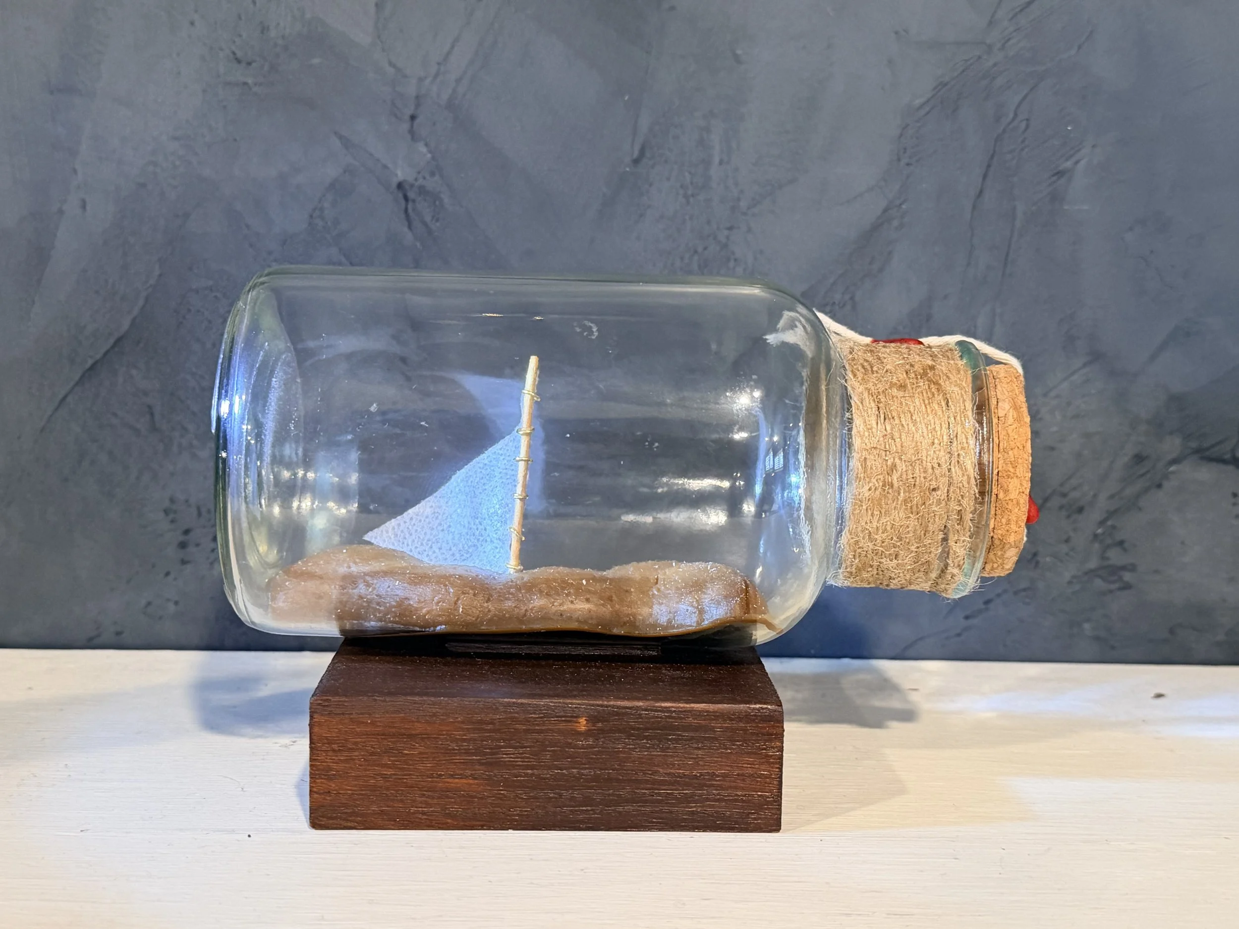 A clear glass jar with a cork lid, placed on a small wooden block, against a dark background.