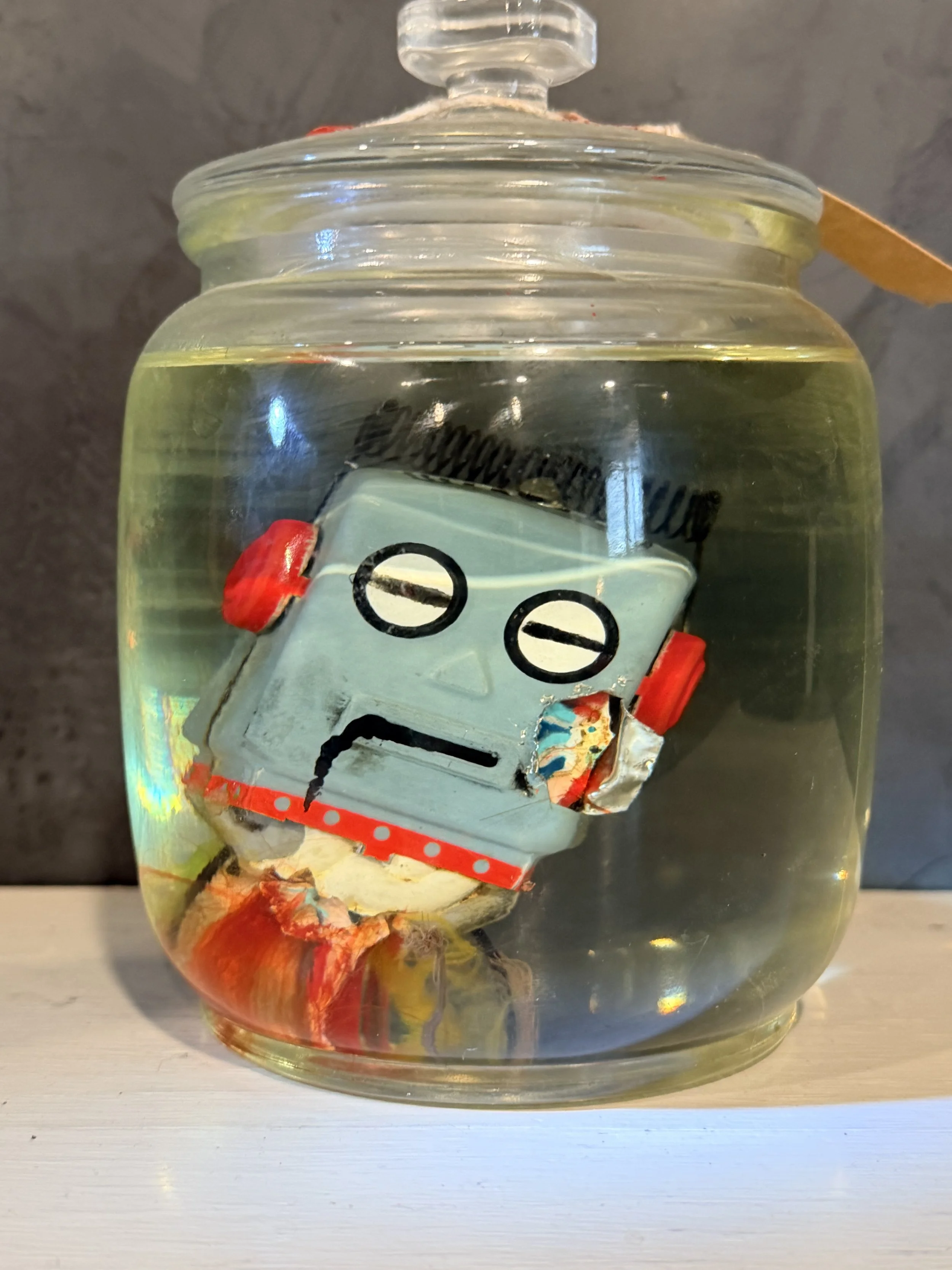 Glass jar filled with water containing a small robot figure submerged and visible through the transparent glass.