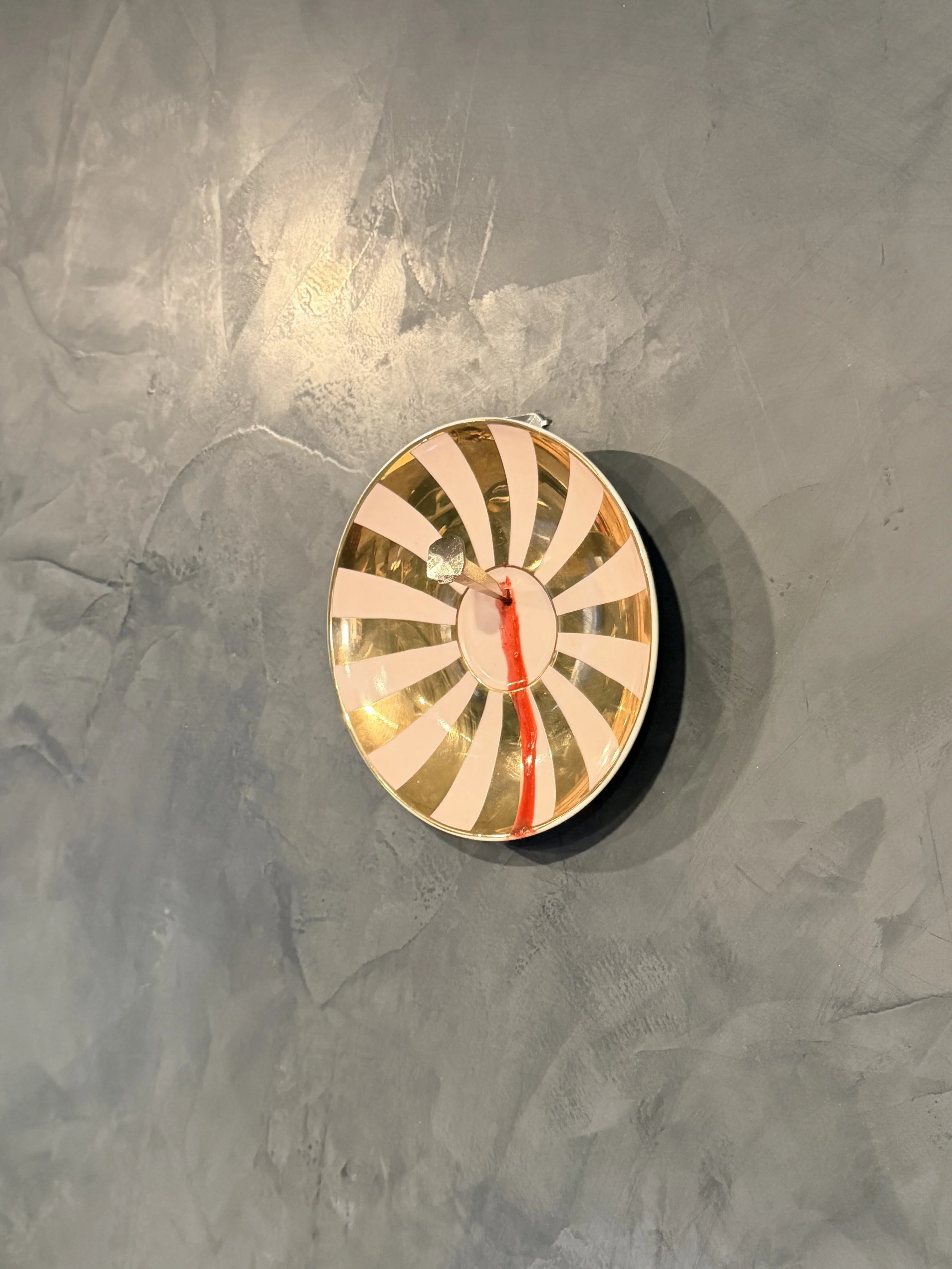 A decorative round mirror with a gold rim and pink rays extending from the center, placed on a dark gray textured surface.