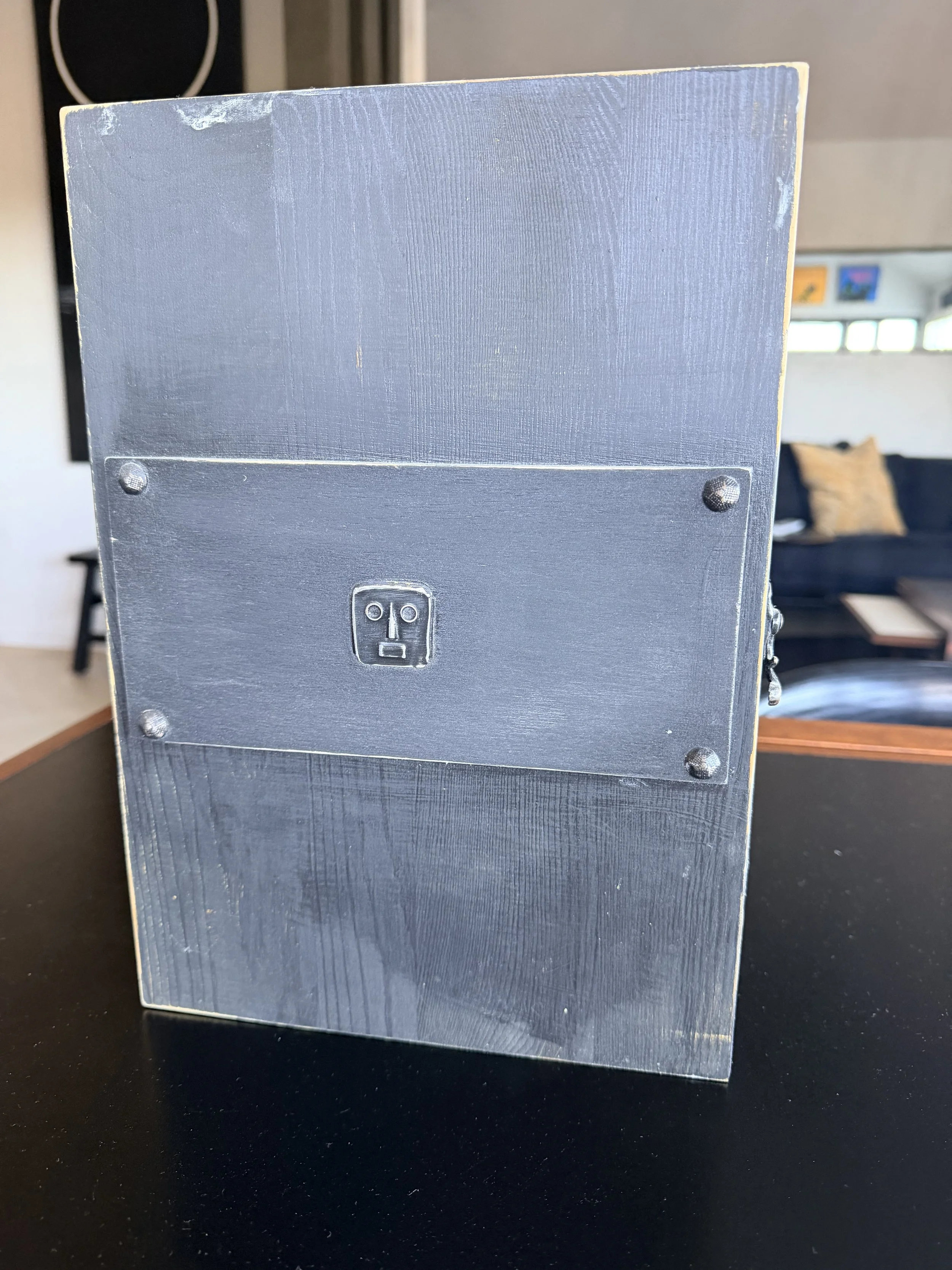 Close-up of a black wooden table with a gray metal electrical outlet attached to a black box, items blurred in the background.