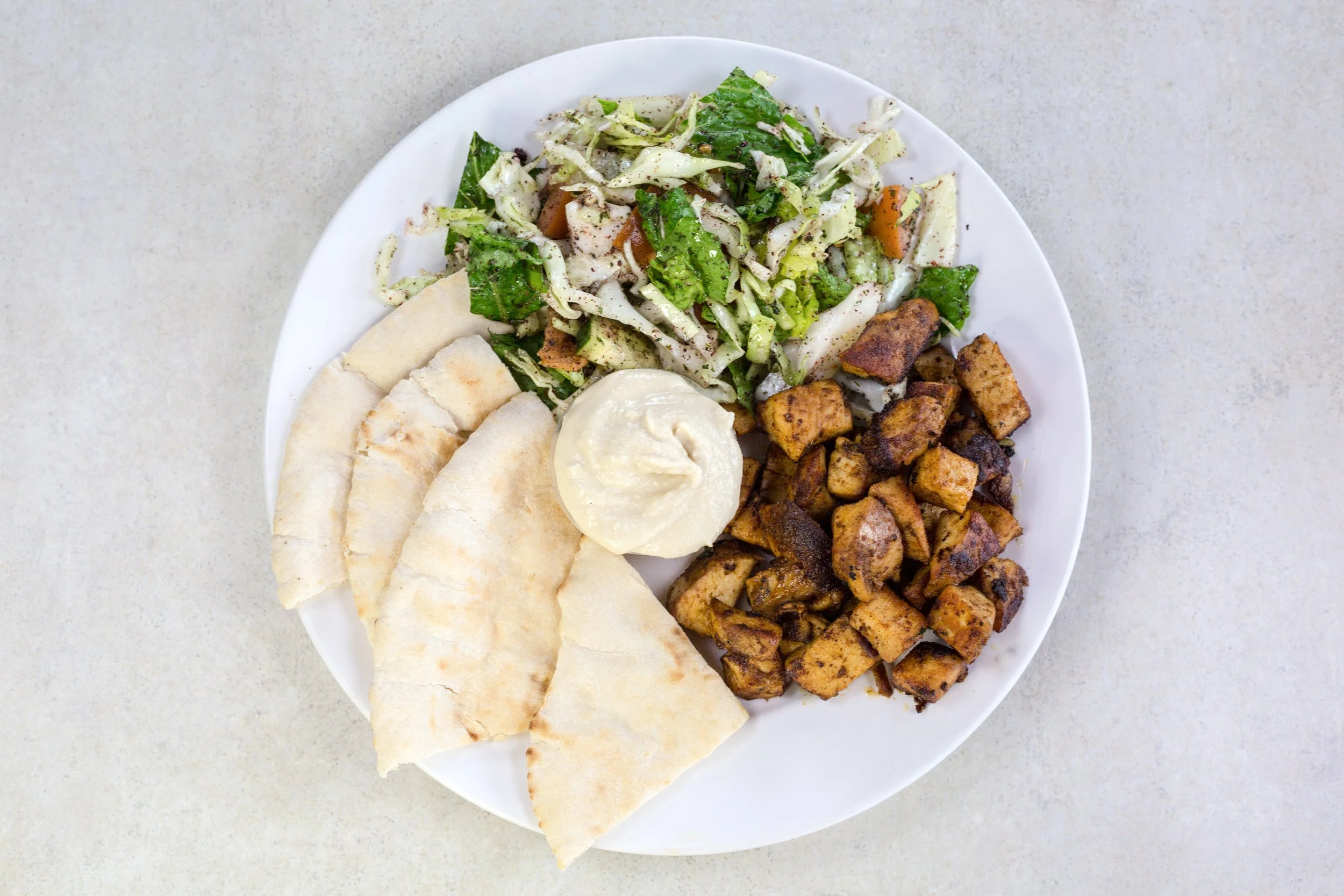 Plate of chopped grilled chicken, flatbread, potato salad, and a side of shredded lettuce with vegetables, all on a white plate.