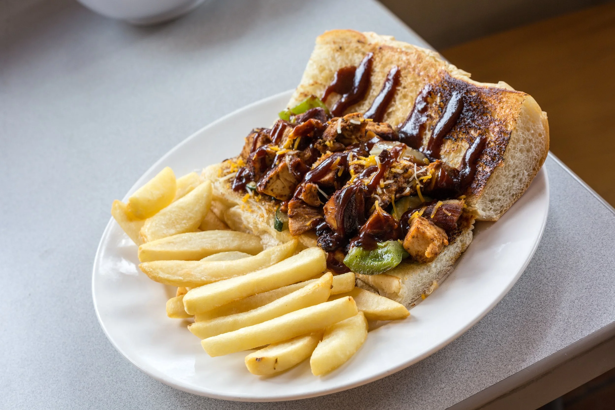 Philly cheesesteak sandwich with french fries on a white plate.