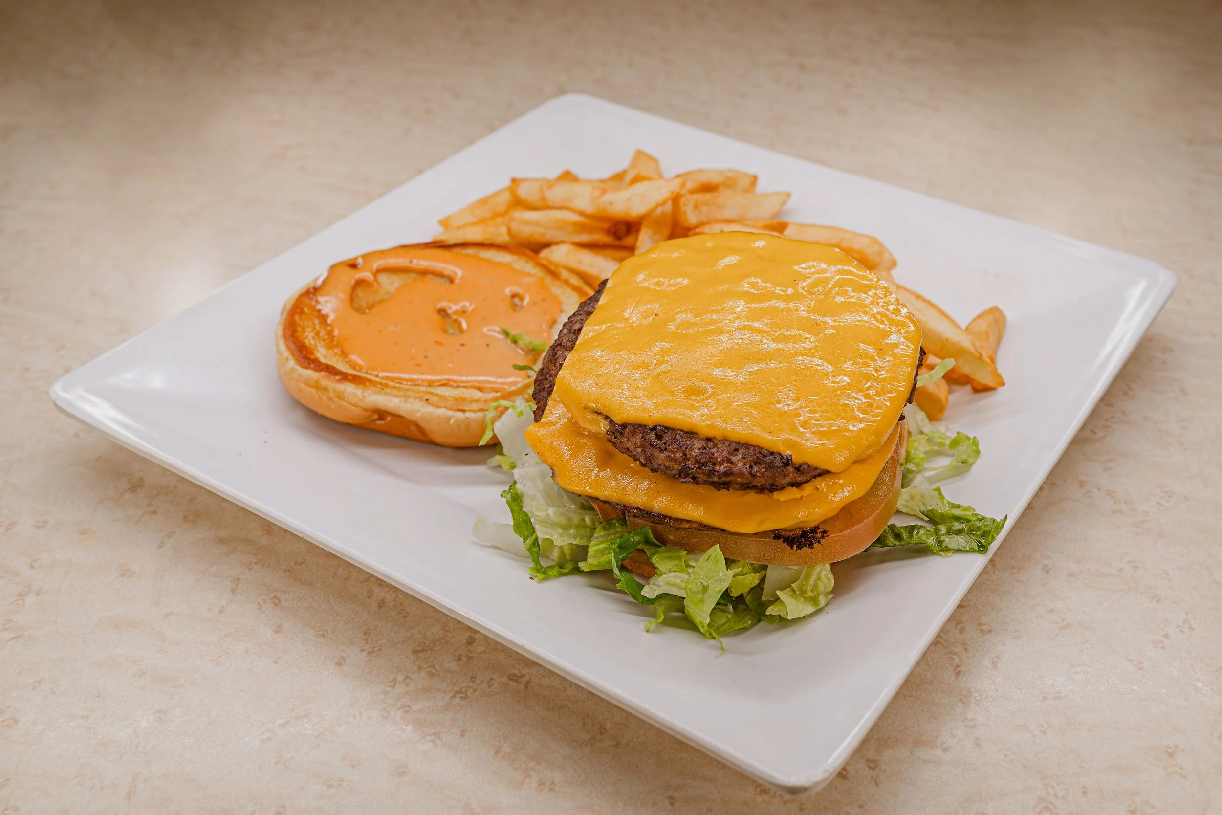 Cheeseburger with cheddar cheese, lettuce, tomato, and ketchup on a bun, served with a side of French fries on a white plate.