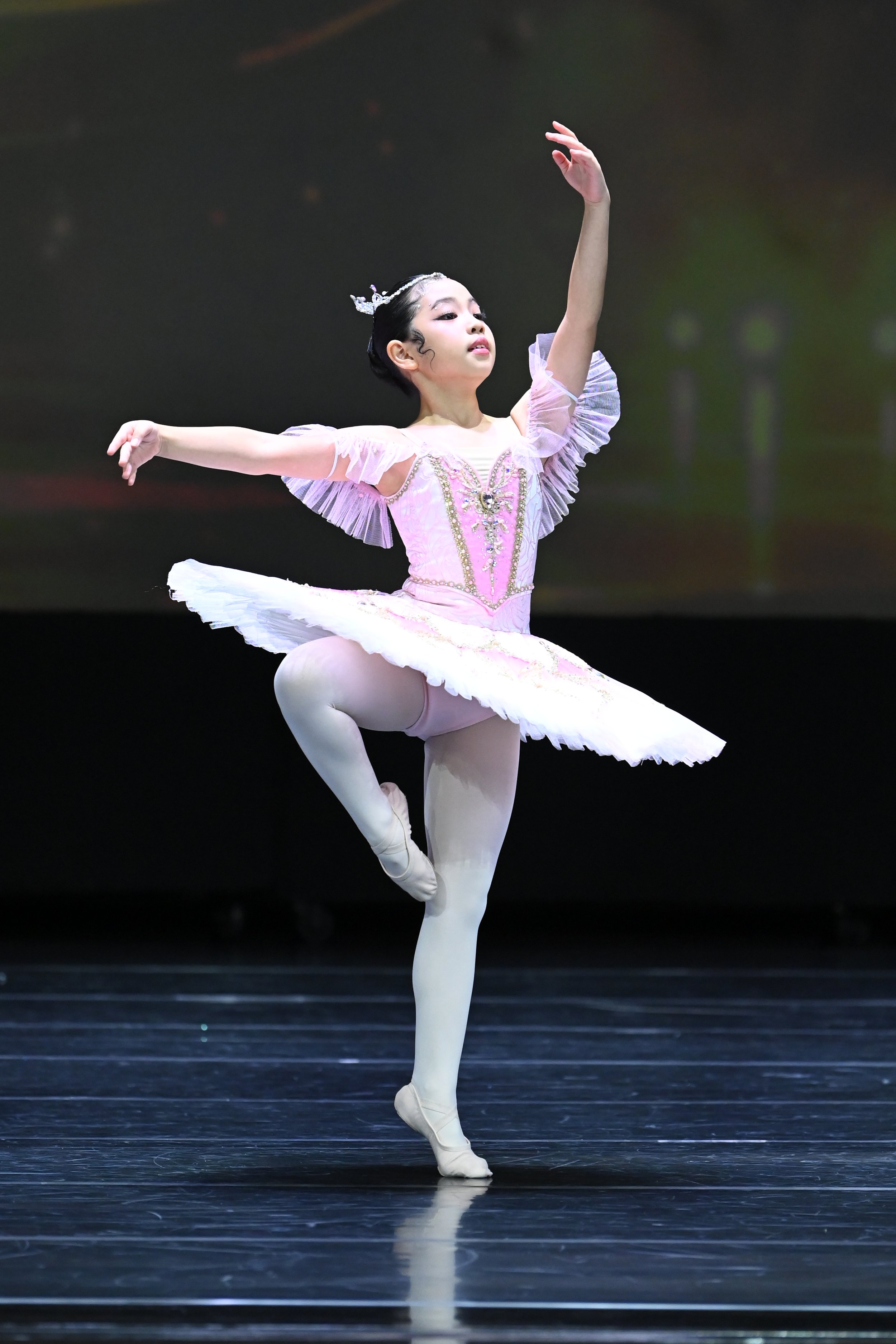 A young female ballet dancer in a pink tutu performing a ballet pose on stage.