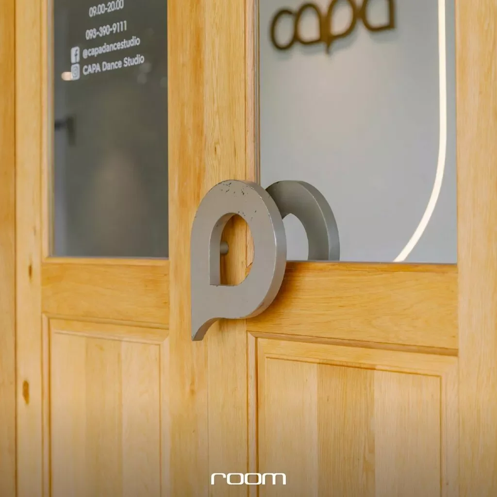 A wooden door with a glass panel and a silver 'P' shaped door handle. There are signs on the glass panel including contact information and social media details for CAPA Dance Studio.