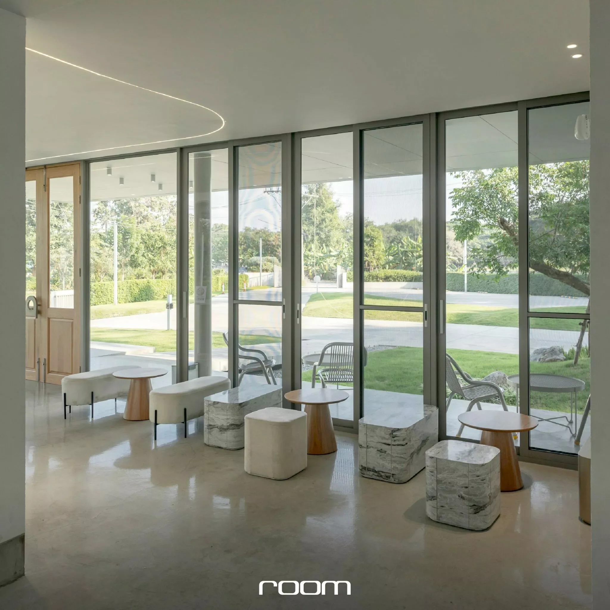 Modern interior with marble seating, chairs, and large glass windows showing greenery outside.