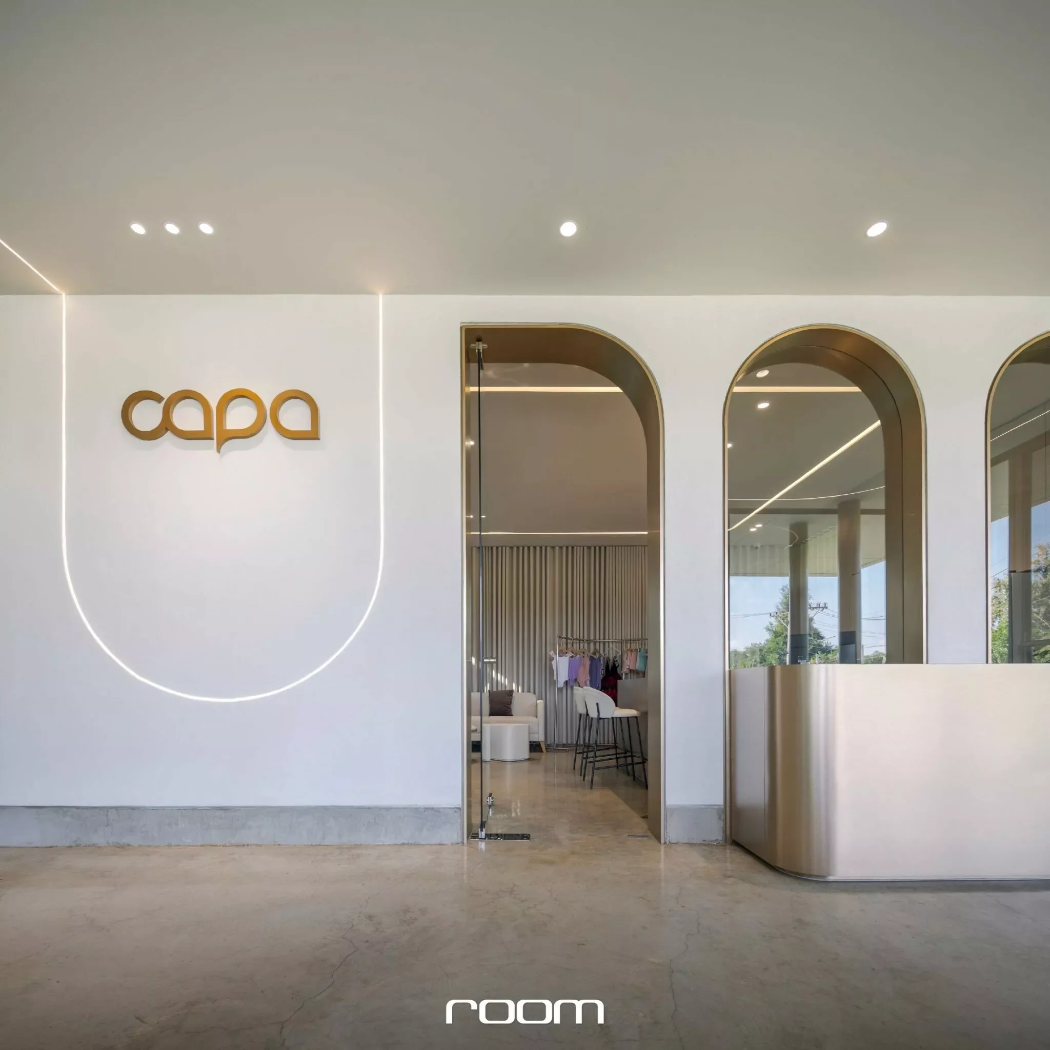Interior view of a modern, minimalist room with neutral tones, large curved mirrors, and a sign that reads 'capa' on the wall.