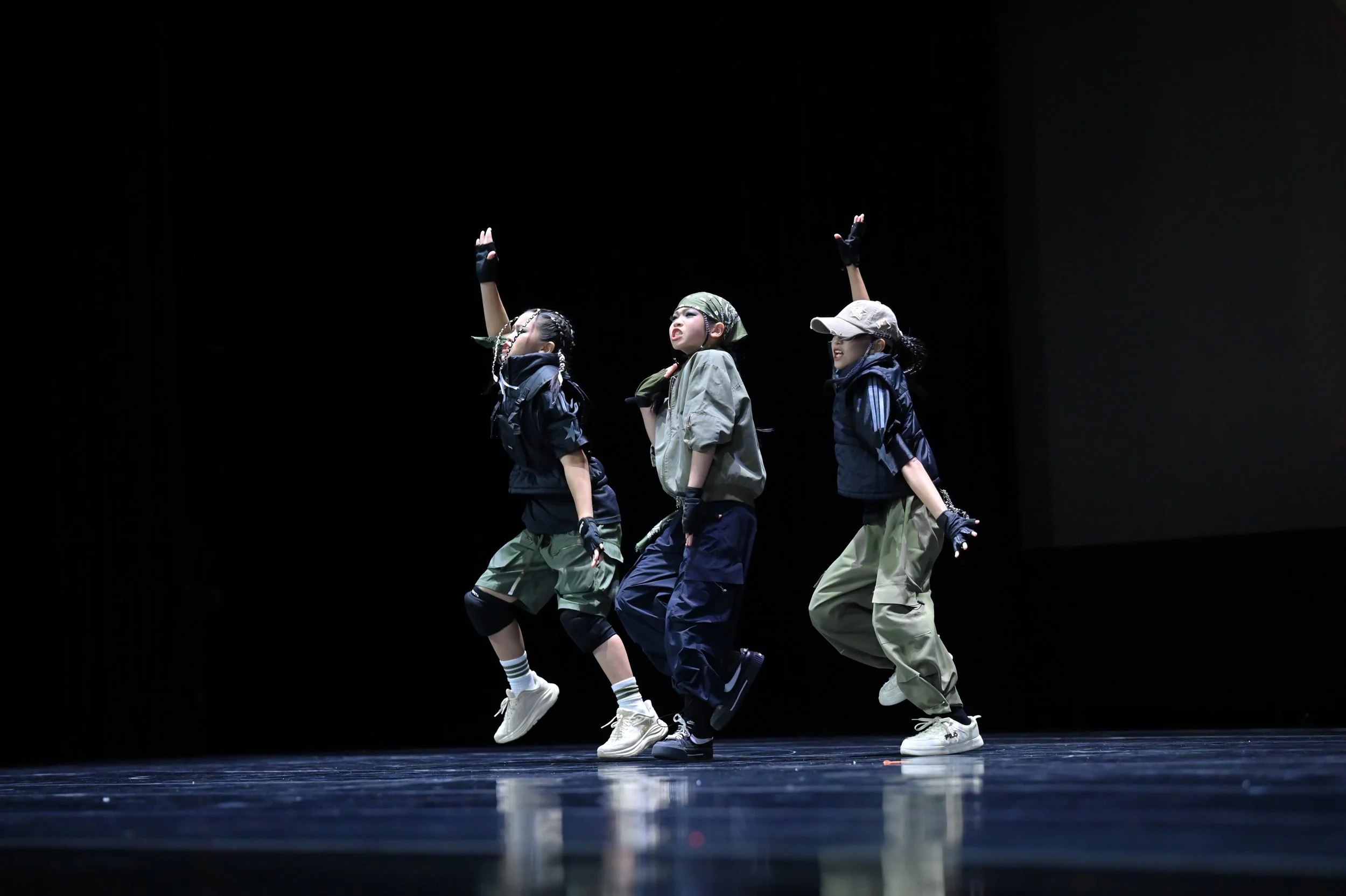 Four young dancers performing on stage, dressed in casual streetwear, with a black background.