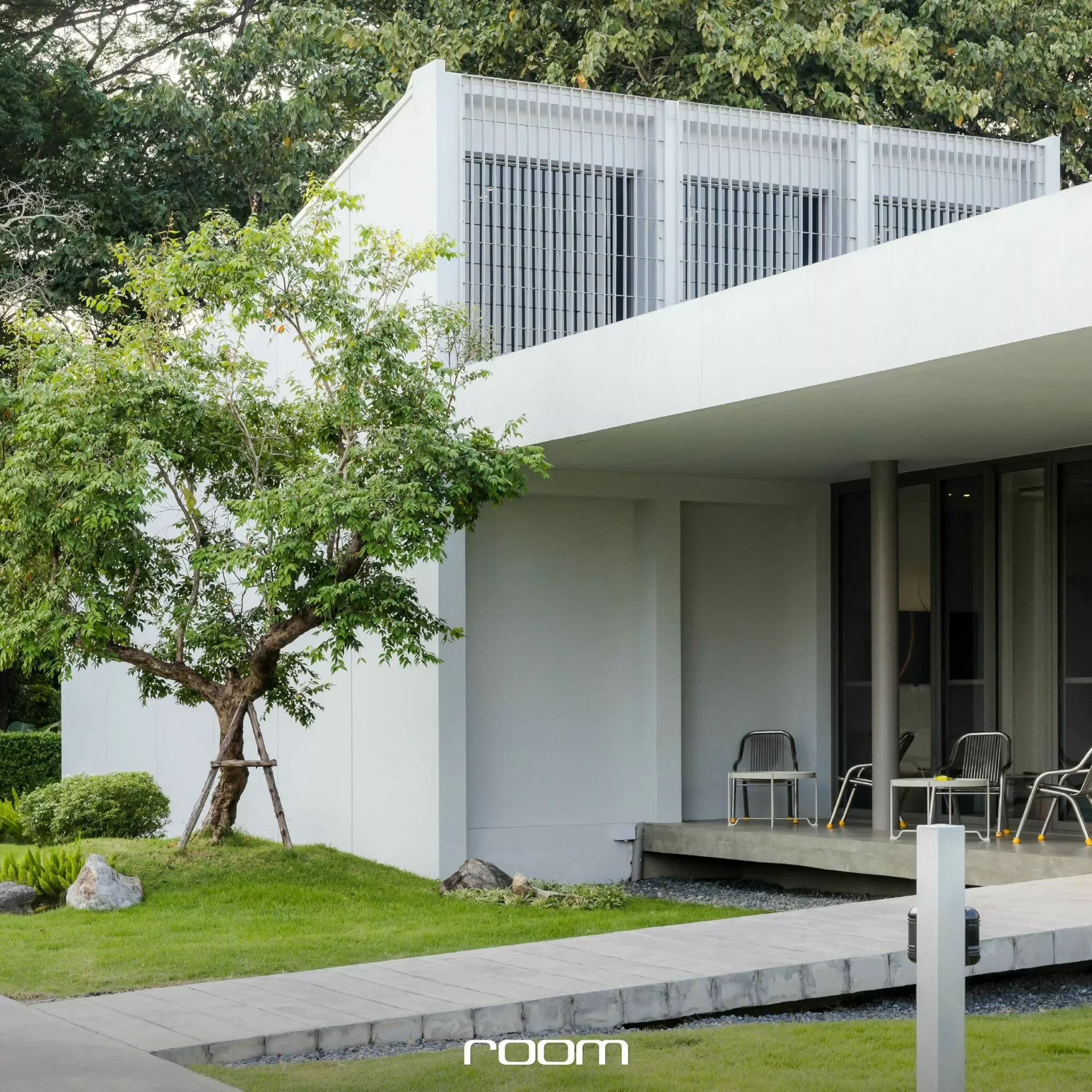 Modern white house with large patio, trees, green lawn, chairs, and architectural details.