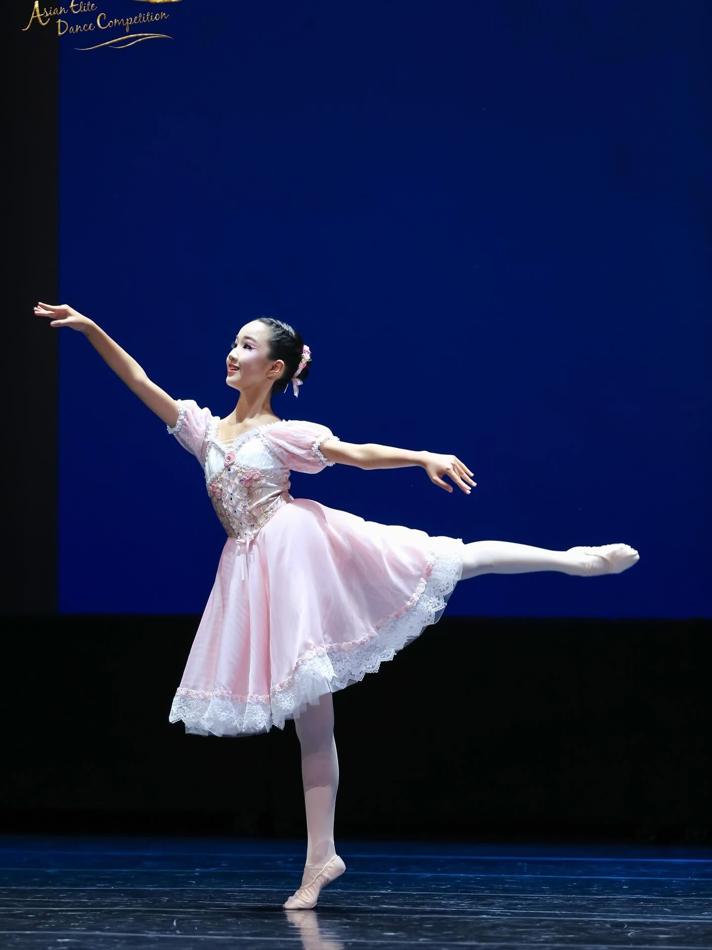 A female ballet dancer in a pink tutu performing an arabesque on stage.