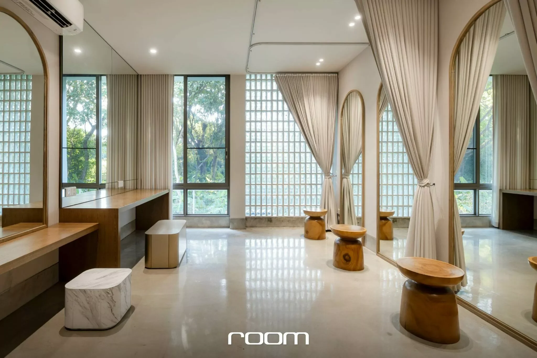 Modern living room with large windows, beige curtains, wooden furniture, and mirrors on the walls.