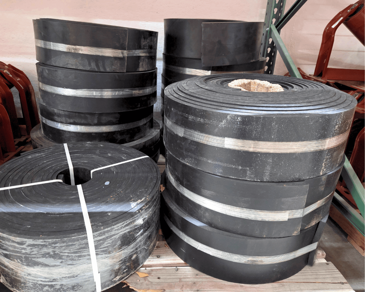 Large black industrial rubber rolls stacked on a wooden pallet in a warehouse
