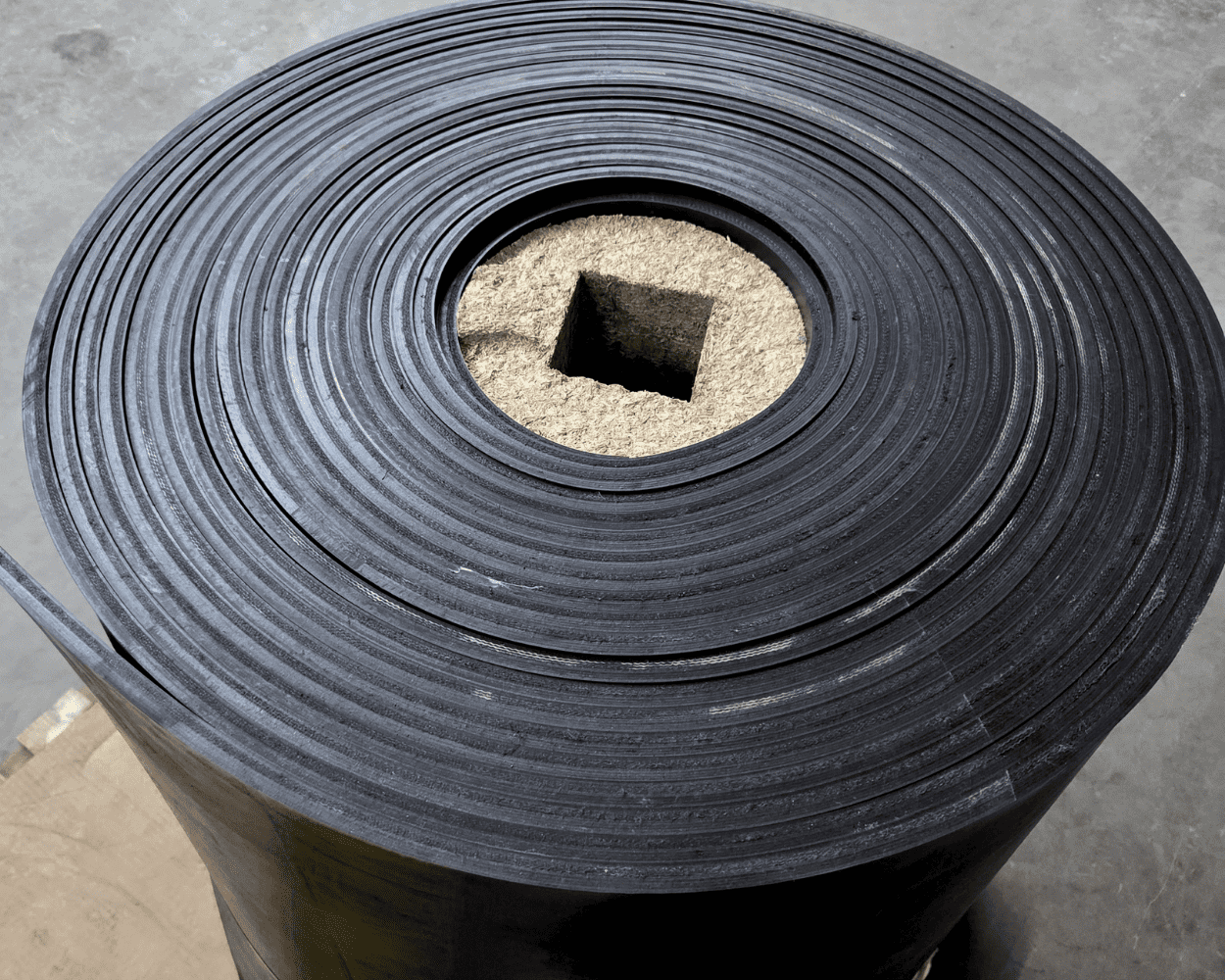 Large roll of black ribbed rubber conveyor belt with a cardboard core.