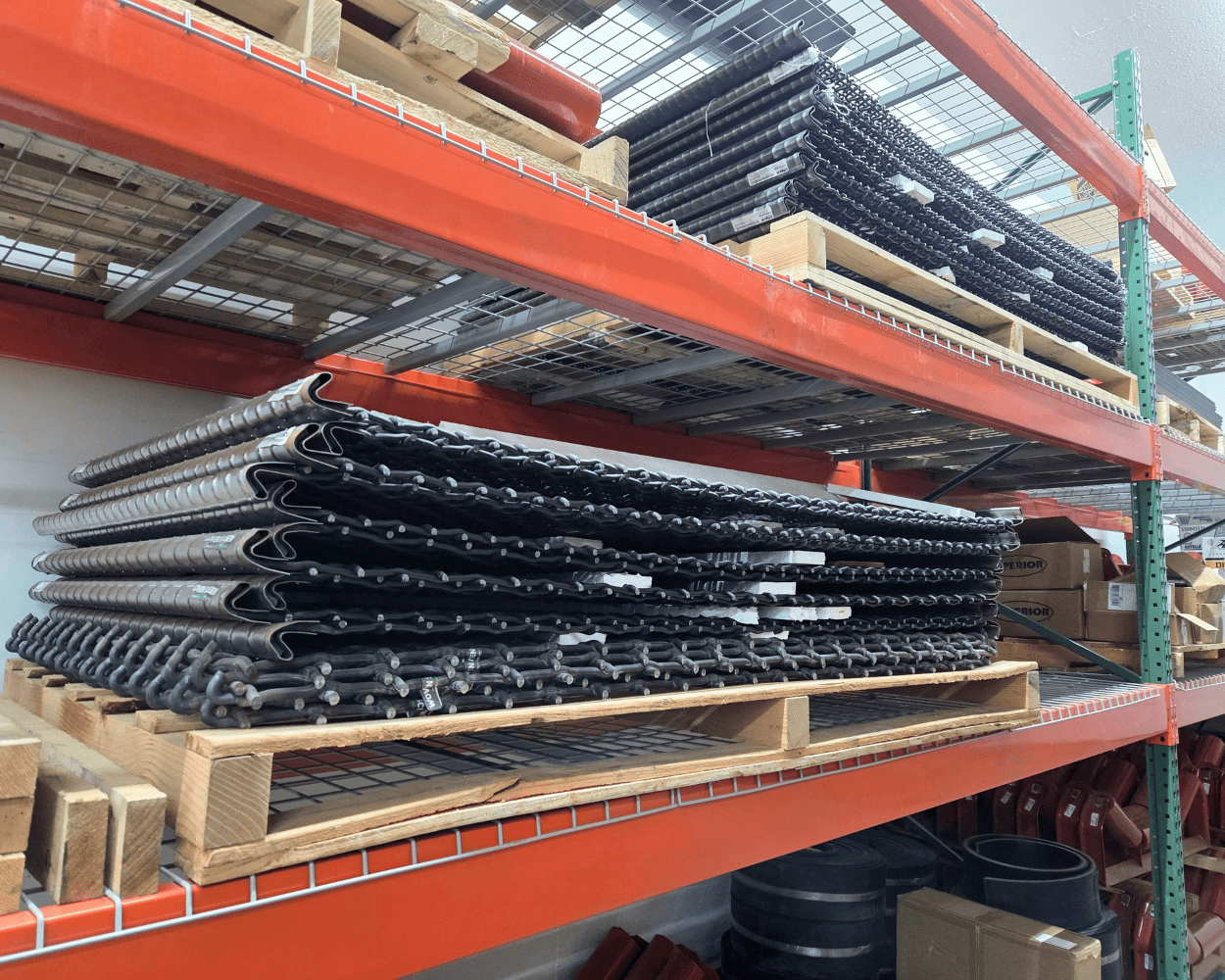Stacks of black rubber conveyor belts stored on wooden pallets in industrial warehouse shelving