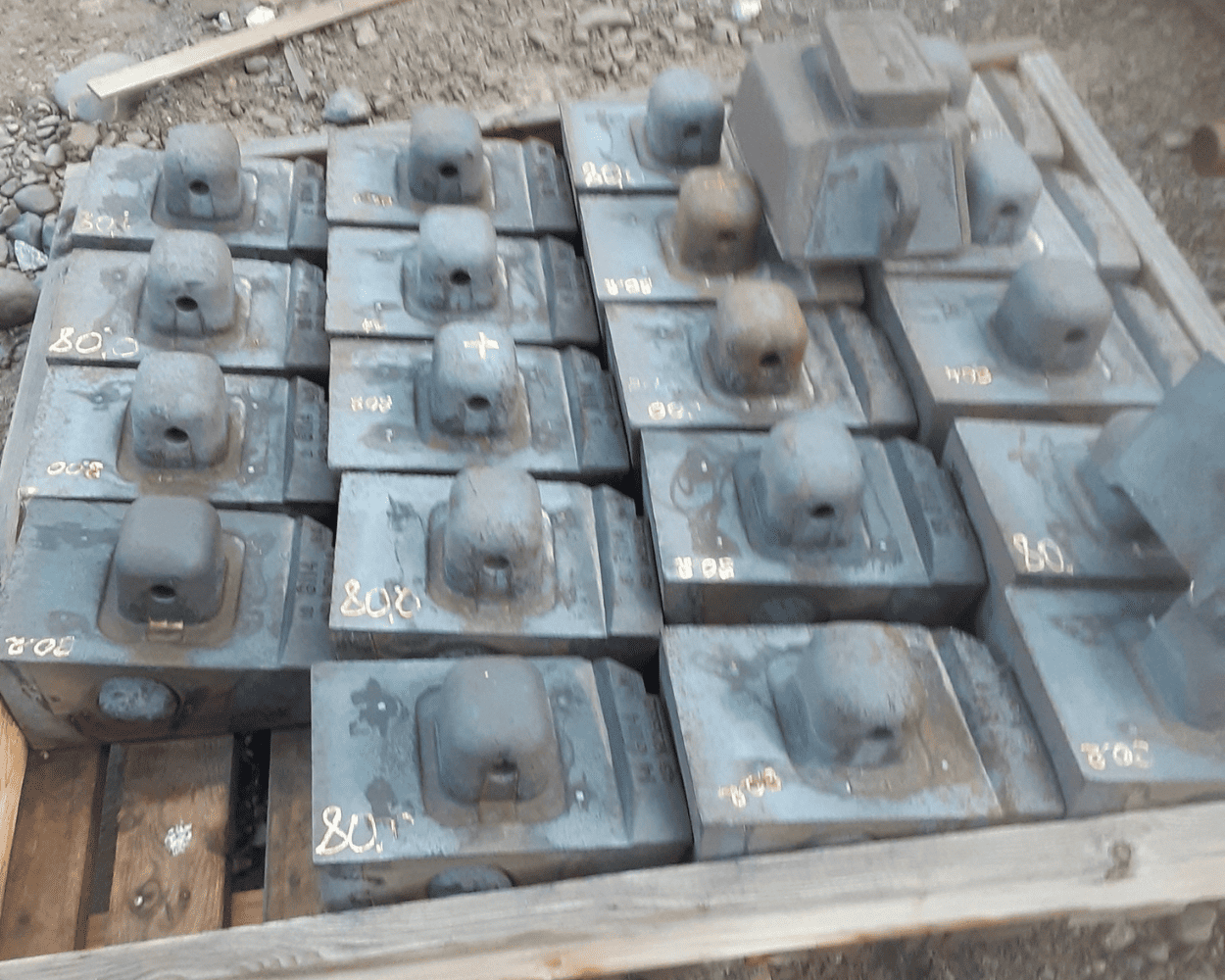 Rows of weathered metal railway tie plates with raised fastener housings and handwritten markings