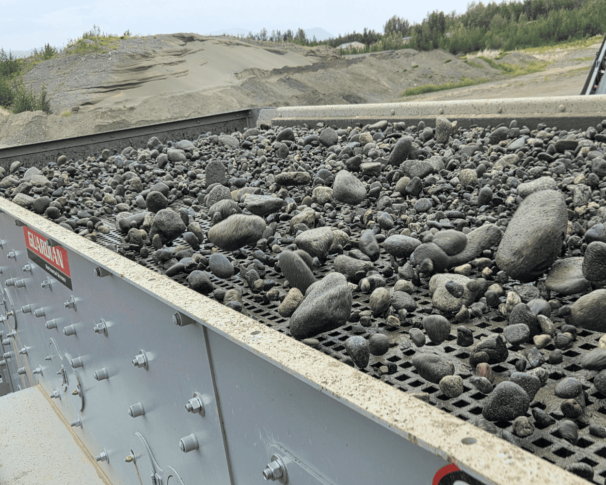 Industrial conveyor screen sorting rounded rocks at a gravel processing site