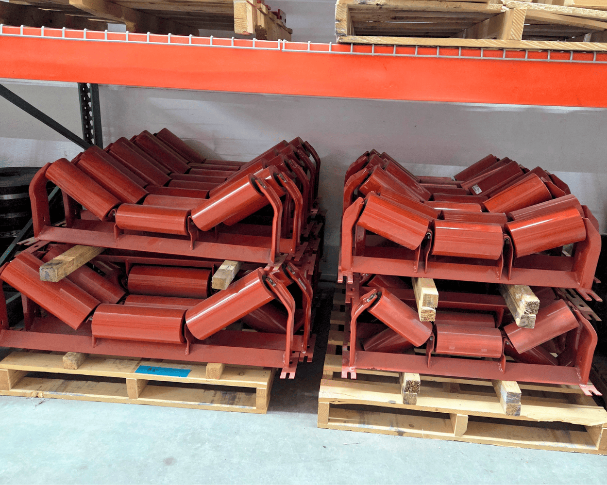 Stacked red conveyor belt rollers on wooden pallets in a warehouse