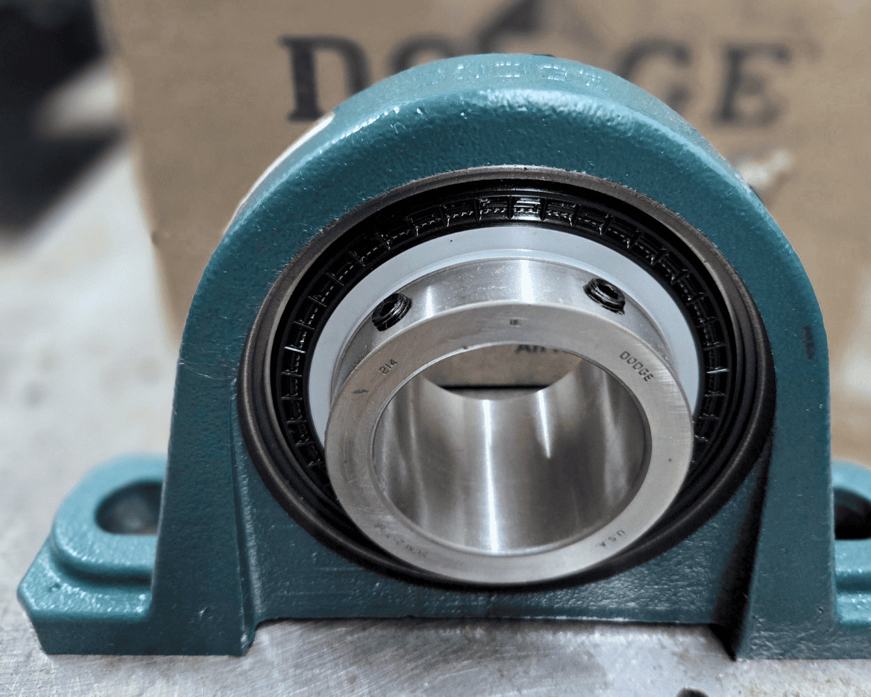 Close-up of a teal industrial pillow block bearing with a stainless steel housing and black seal