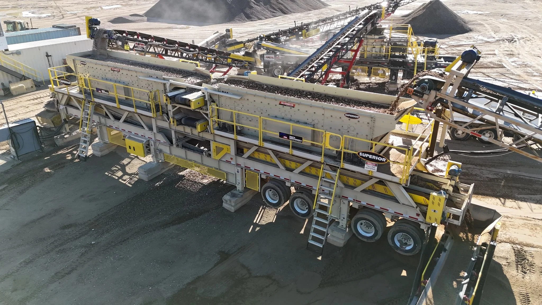 Mobile rock-crushing and screening plant processing gravel at an aggregate quarry with conveyor belts and stockpiles.