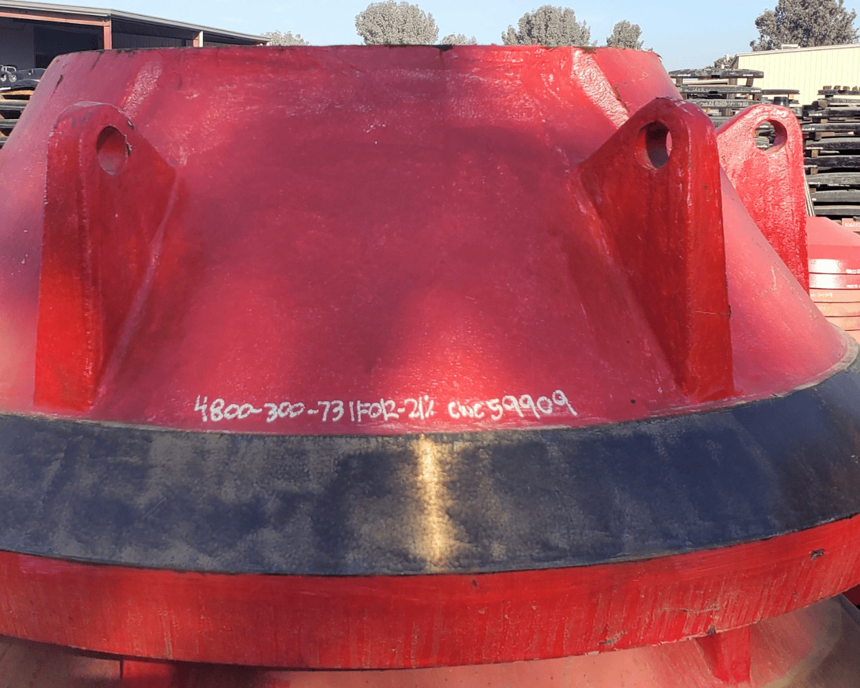 Close-up of a red heavy-duty excavator bucket with mounting holes and black wear strip