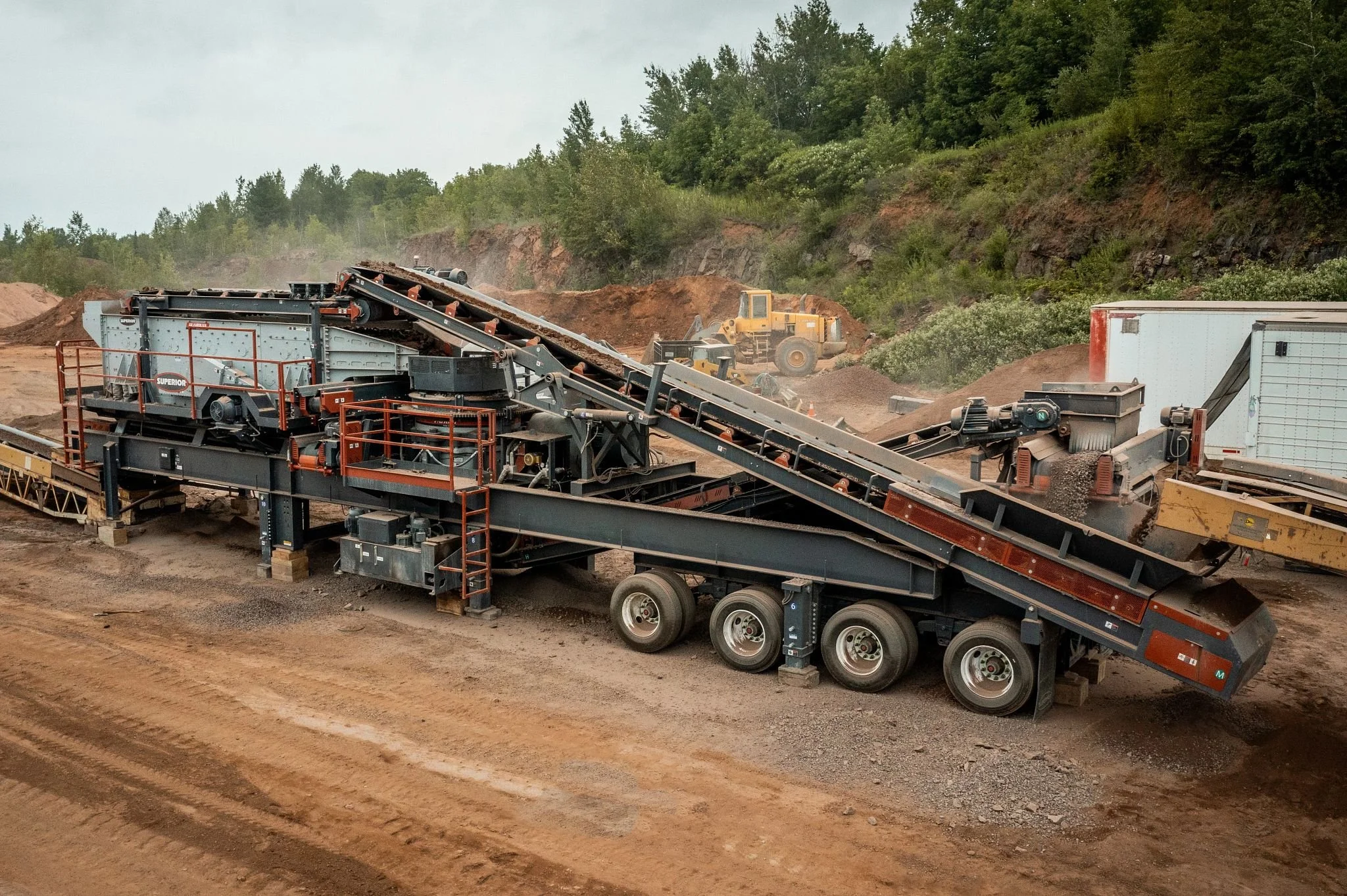 Rock quarry with industrial conveyor belts, a screening plant, loader, and piles of crushed stone.