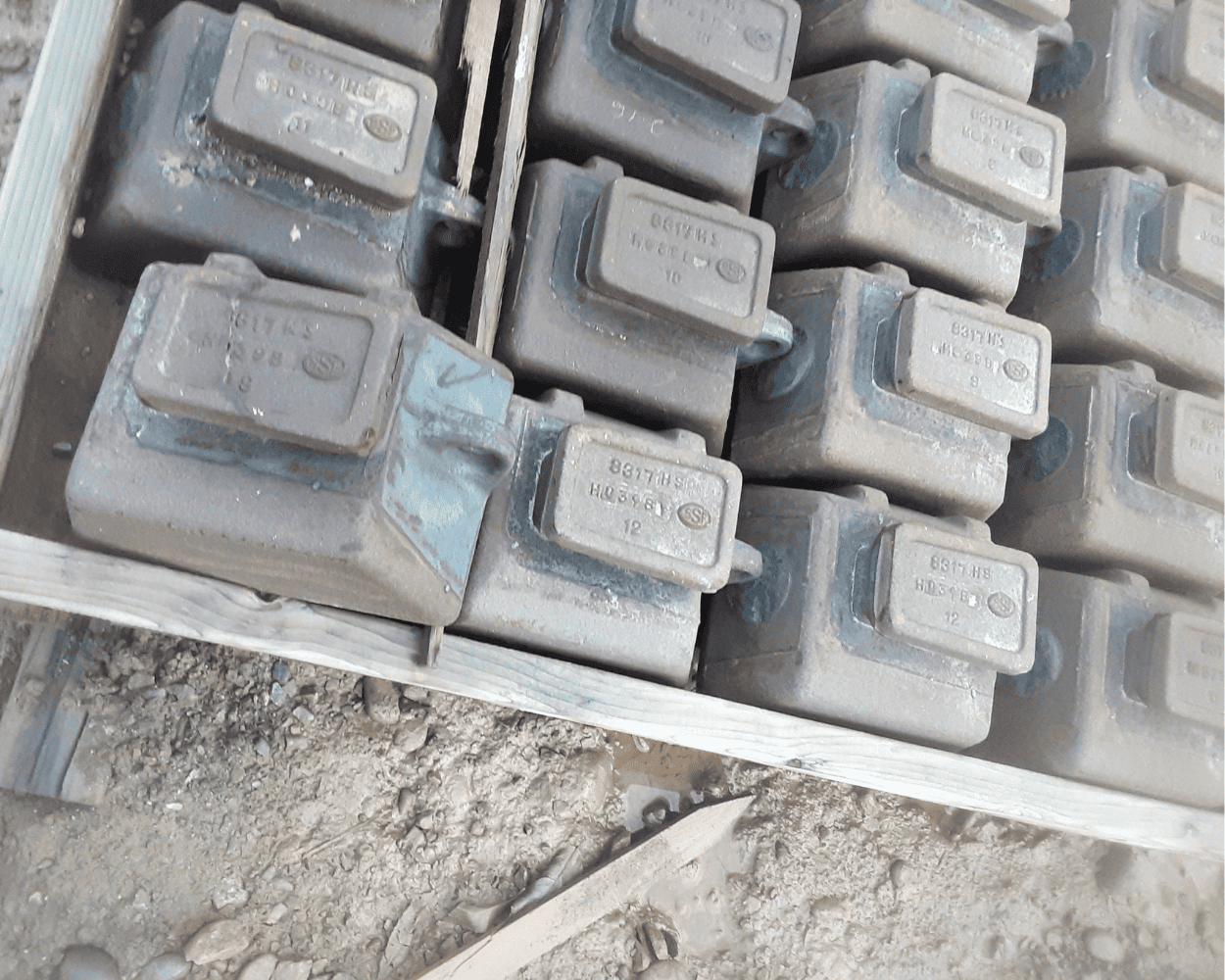 Close-up of dusty metal industrial components with raised identification plates arranged in a crate.
