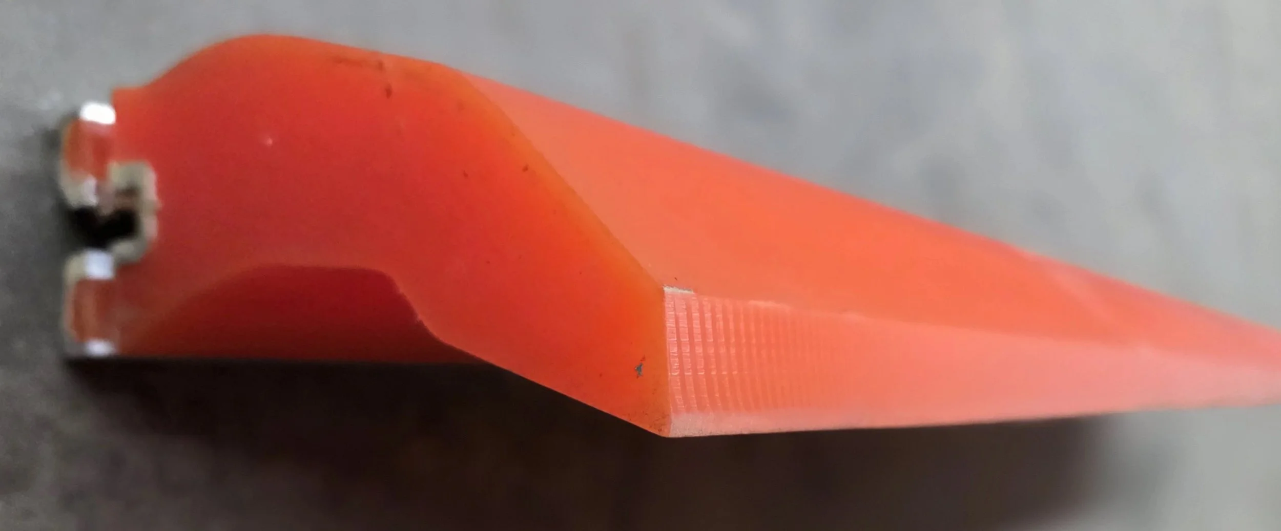 Close-up of an orange-red plastic tool handle with a metal end on a dark surface
