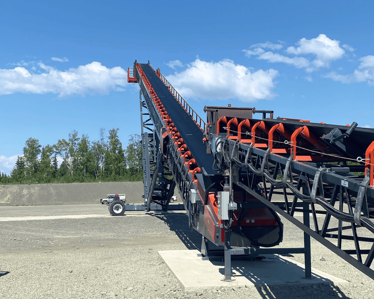 Industrial conveyor system with elevated belt and orange rollers at an outdoor aggregate processing facility